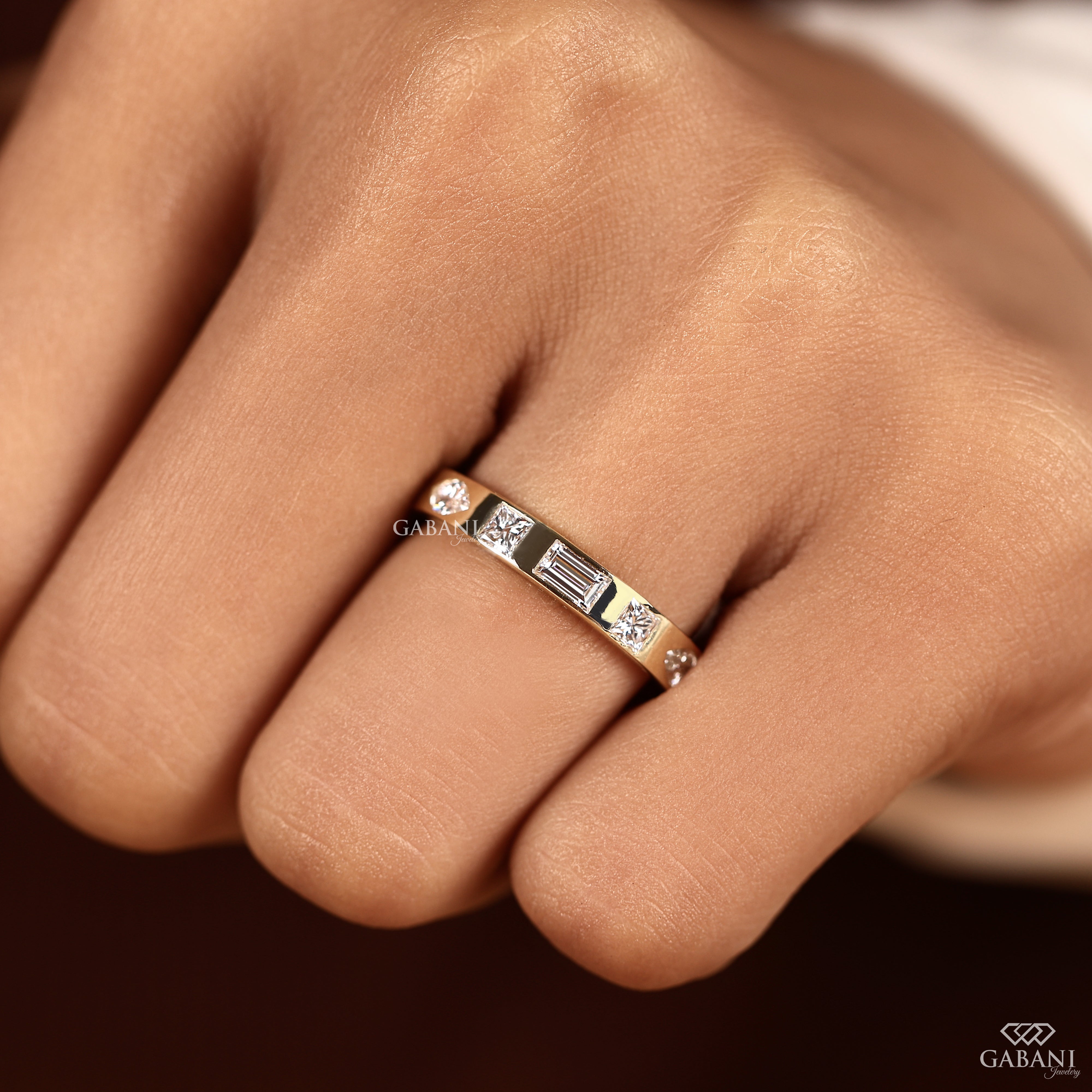 Close view of a flush set lab grown diamond wedding band with mixed diamond shapes in a flat 14K yellow gold band designed for stacking and daily wear.