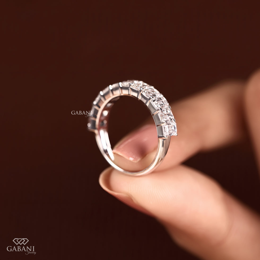 Model holding an emerald cut lab created diamond matching wedding band in white gold between her fingers