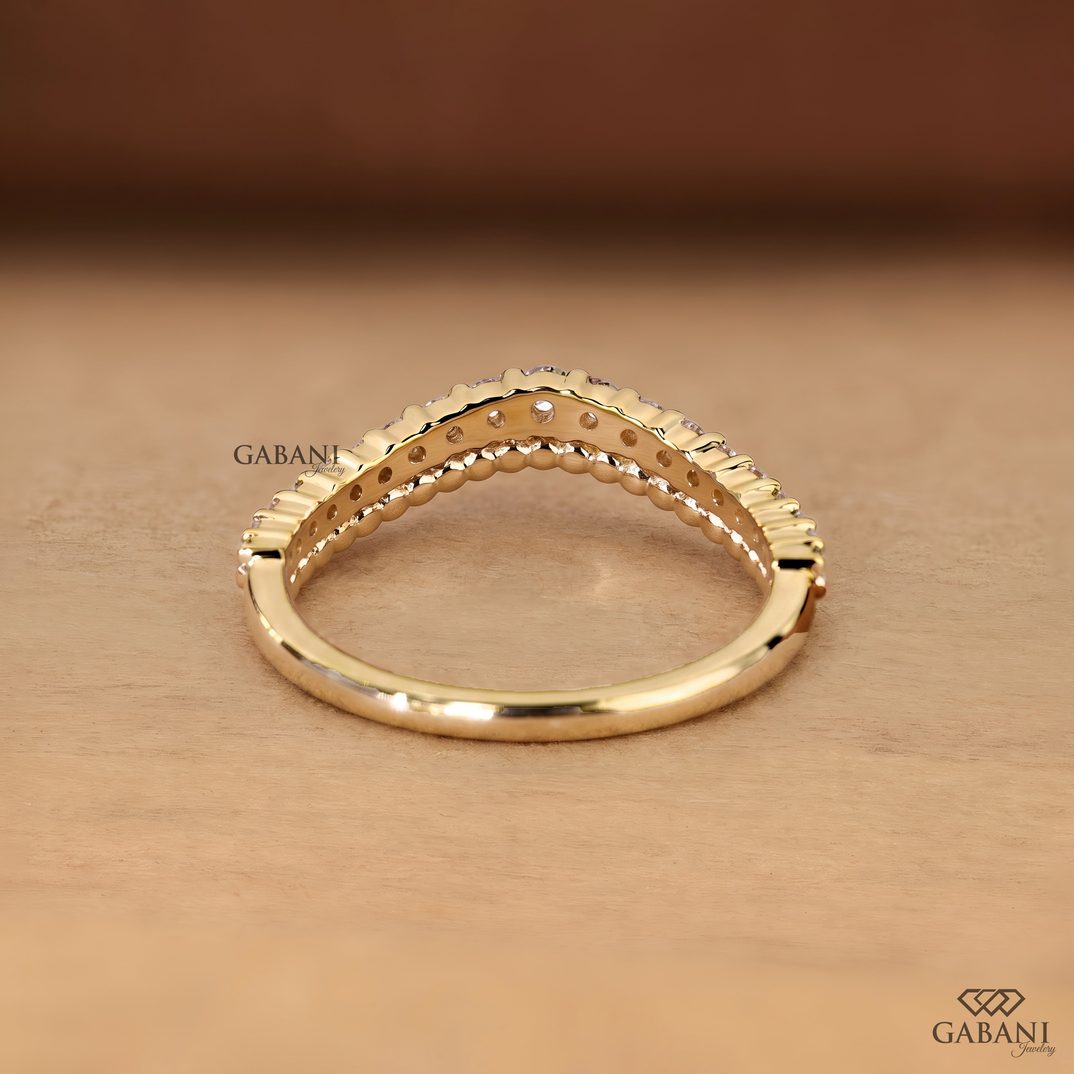 A gold ring with a textured beaded top band and a smooth shank, displayed on a warm brown wooden surface. The brand name 'GABANI' is visible as a watermark.