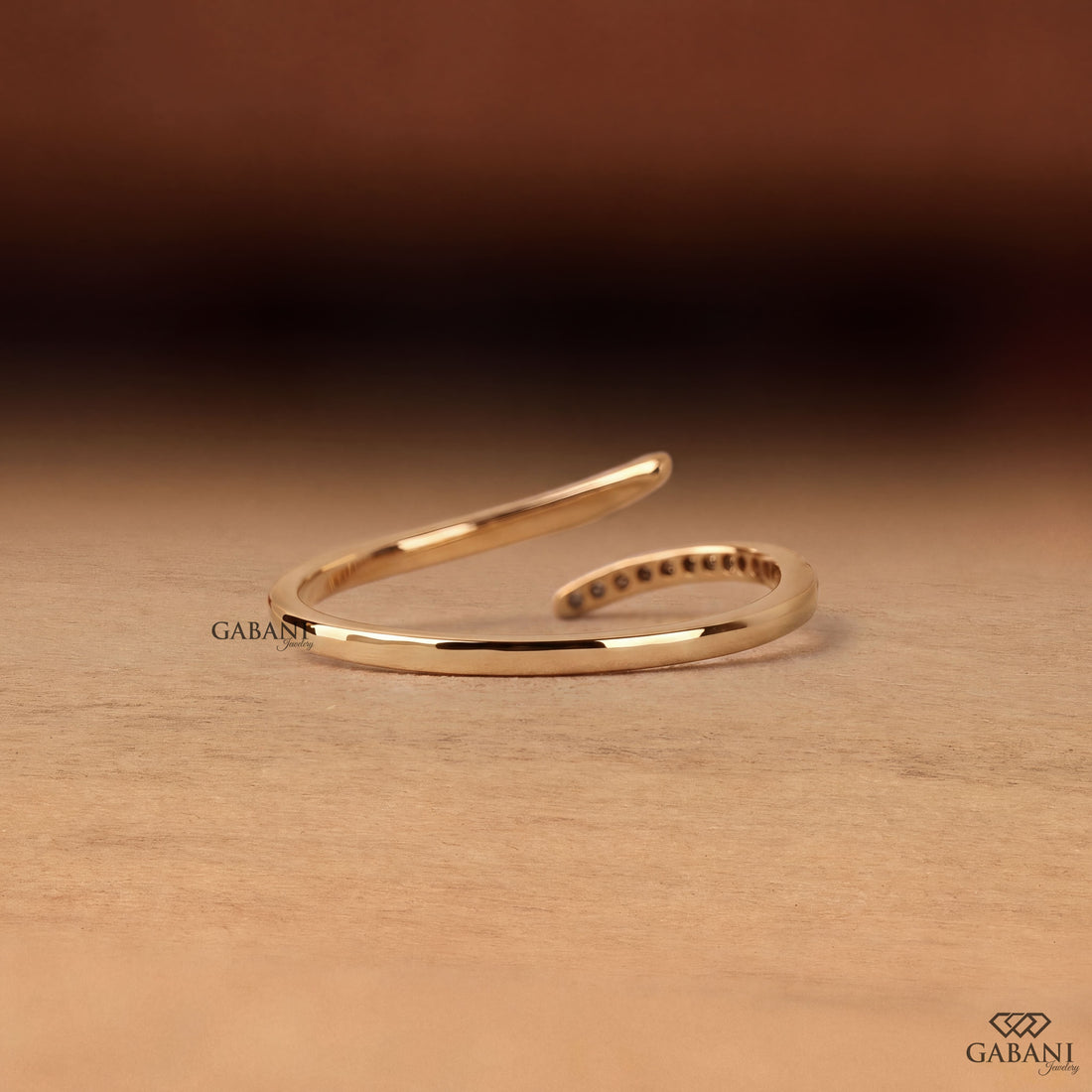 a round lab grown diamond open cuff bangle bracelet in 14K yellow gold, featuring sparkling round diamonds along one curved end and a smooth polished gold wrap design by Gabani Jewelry.