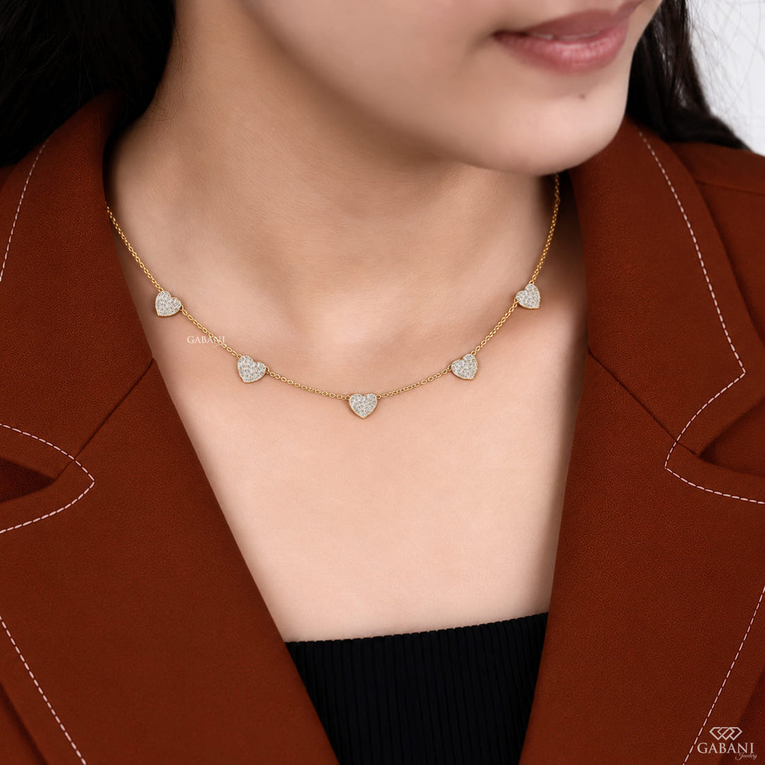 Dainty gold necklace with five sparkling heart charms covered in small round pavé set diamonds on a fine chain.
