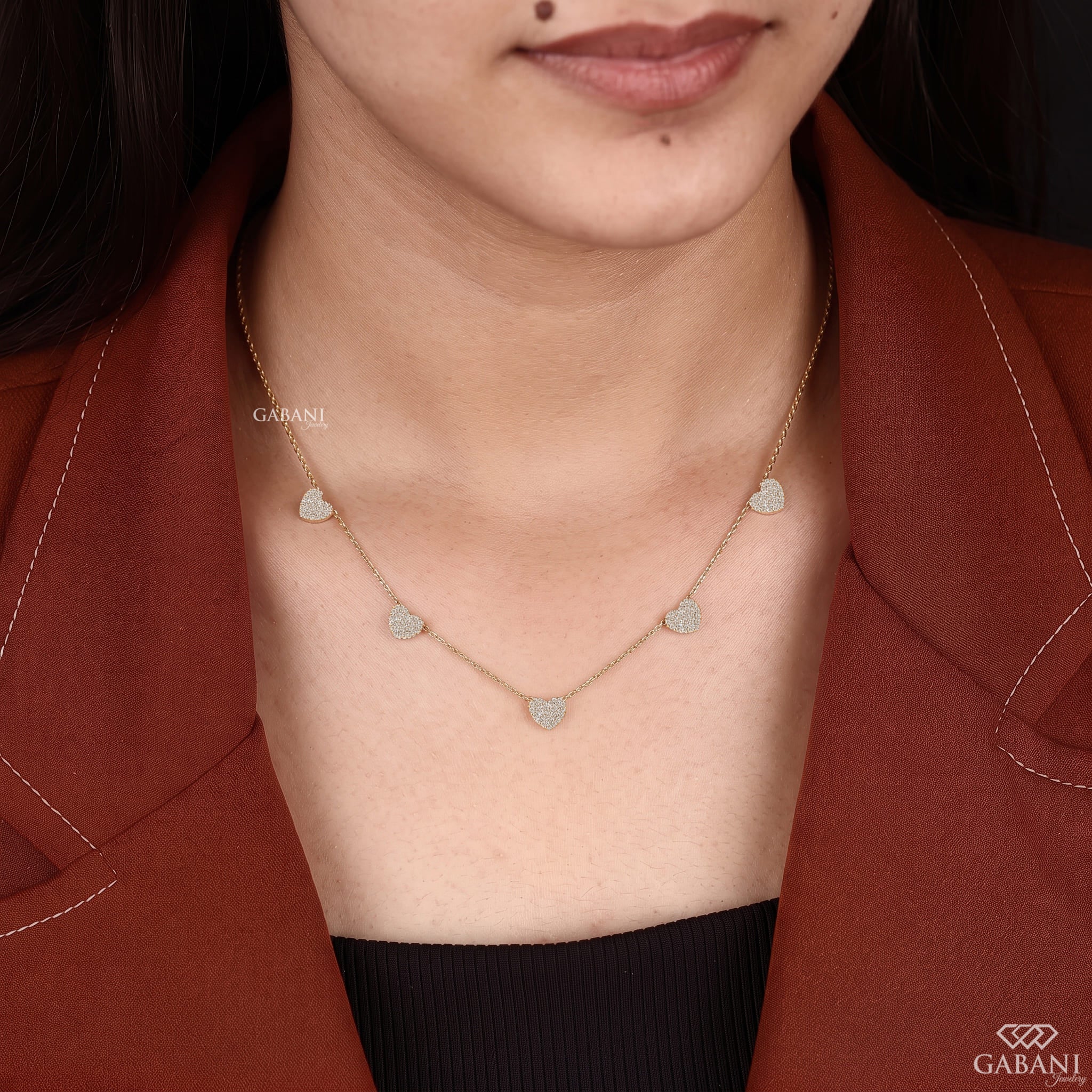 Dainty gold necklace with five sparkling heart charms covered in small round pavé set diamonds on a fine chain.