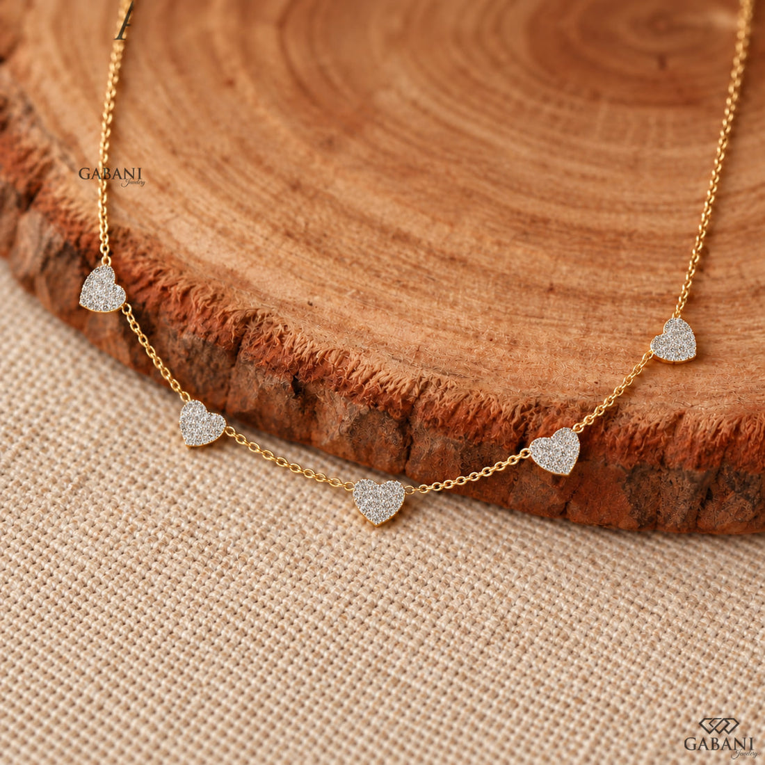 Dainty gold necklace with five sparkling heart charms covered in small round pavé set diamonds on a fine chain.