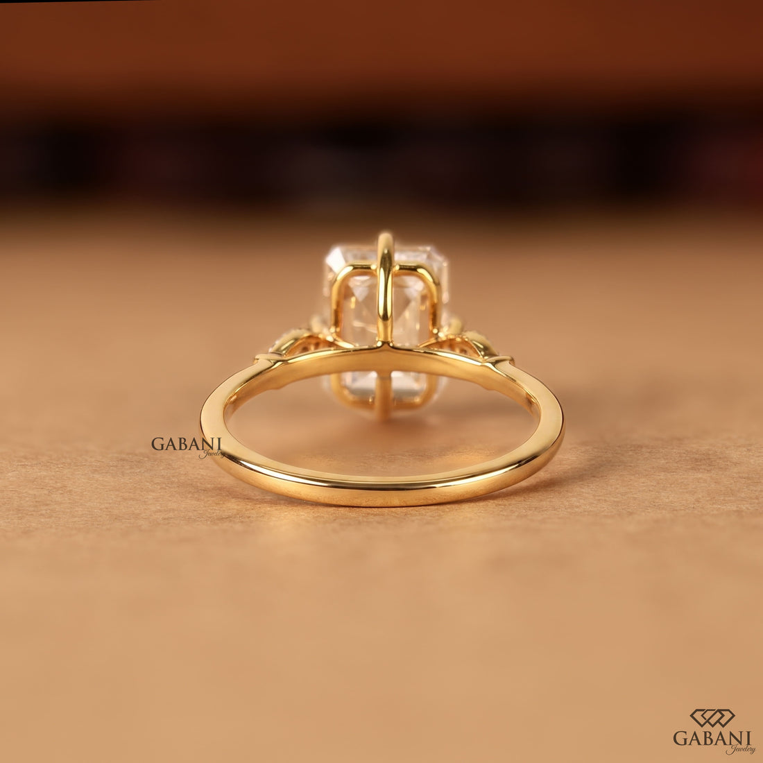 Emerald cut lab grown diamond engagement ring with 9x7mm center stone, four prong setting, and round diamond side accents in 18K gold
