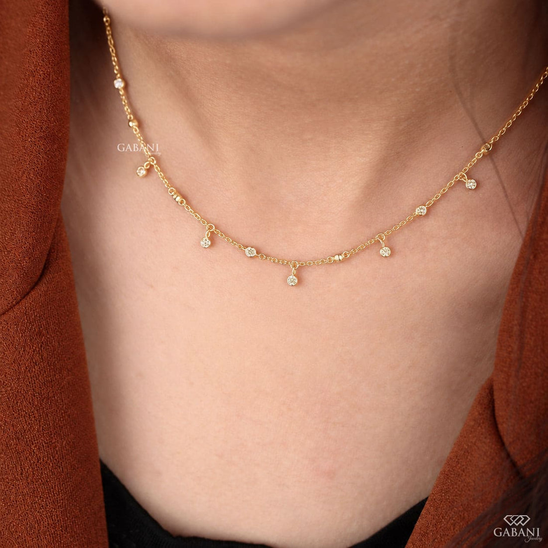Round cut lab grown diamond station necklace with equal size bezel set diamonds and dangling diamond charms in 18K yellow gold.