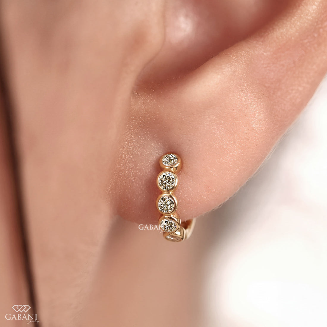 Graduated round diamond bezel huggie earrings in yellow gold with five round diamonds and a hinged hoop closure.
