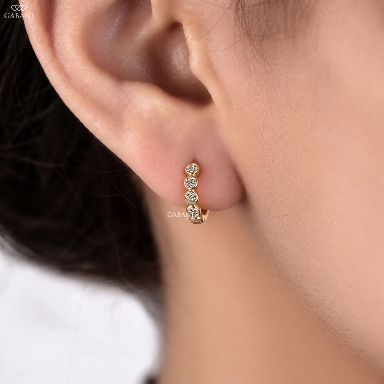 Graduated round diamond bezel huggie earrings in yellow gold with five round diamonds and a hinged hoop closure.