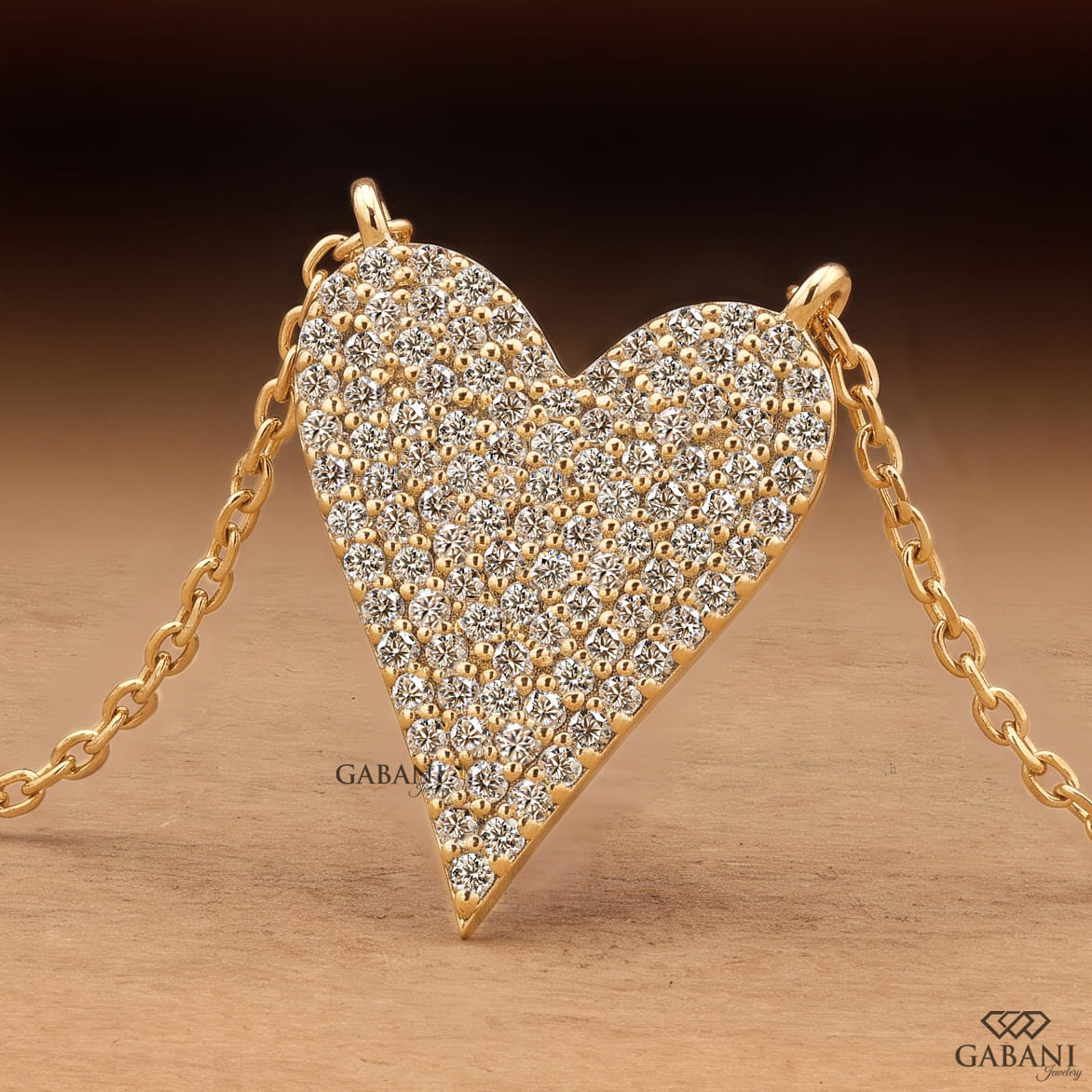 Close-up of an asymmetrical heart shaped lab grown diamond necklace featuring round cut pavé diamonds set in yellow gold.
