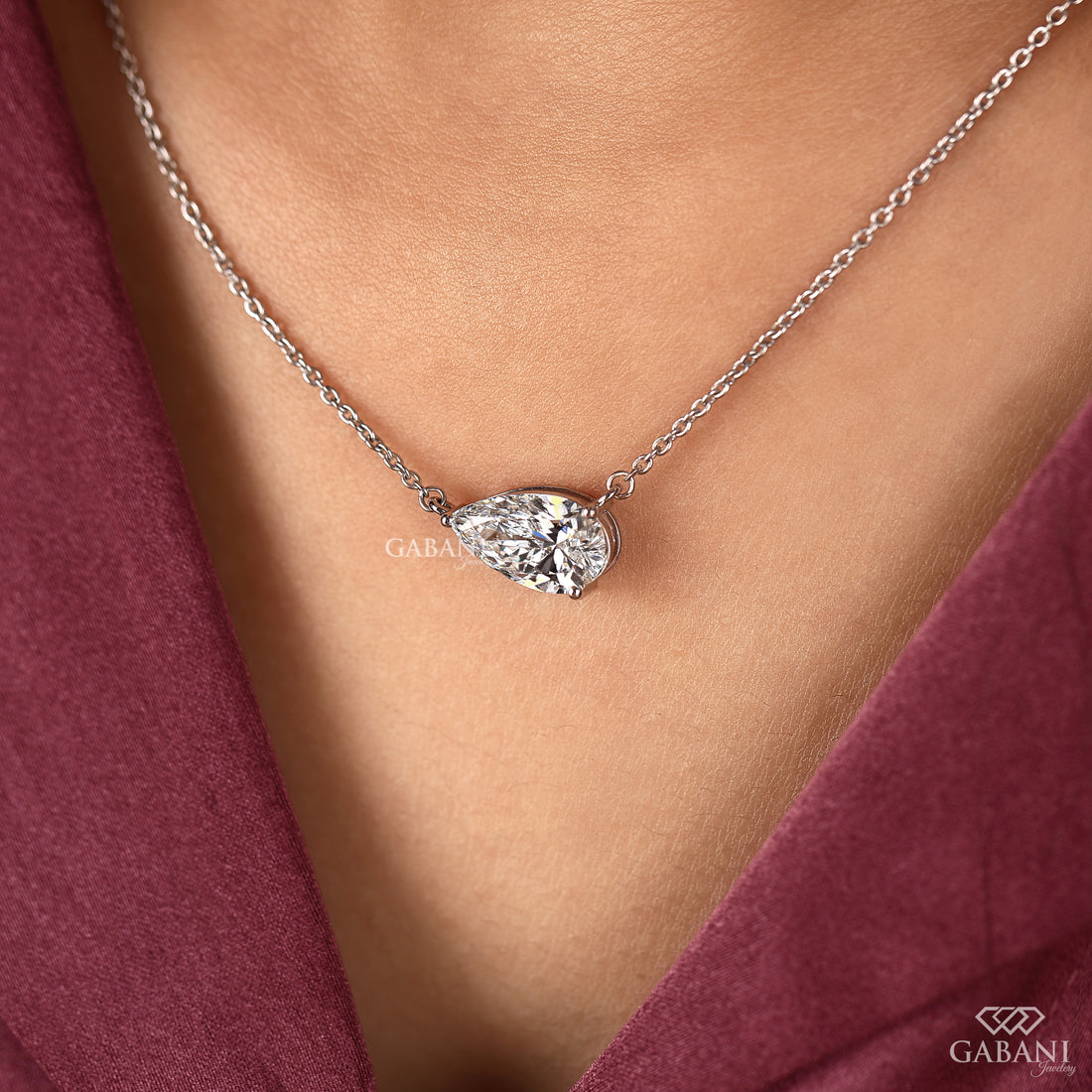 Diamond necklace on a person wearing a burgundy top, with 'GABANI' branding.
