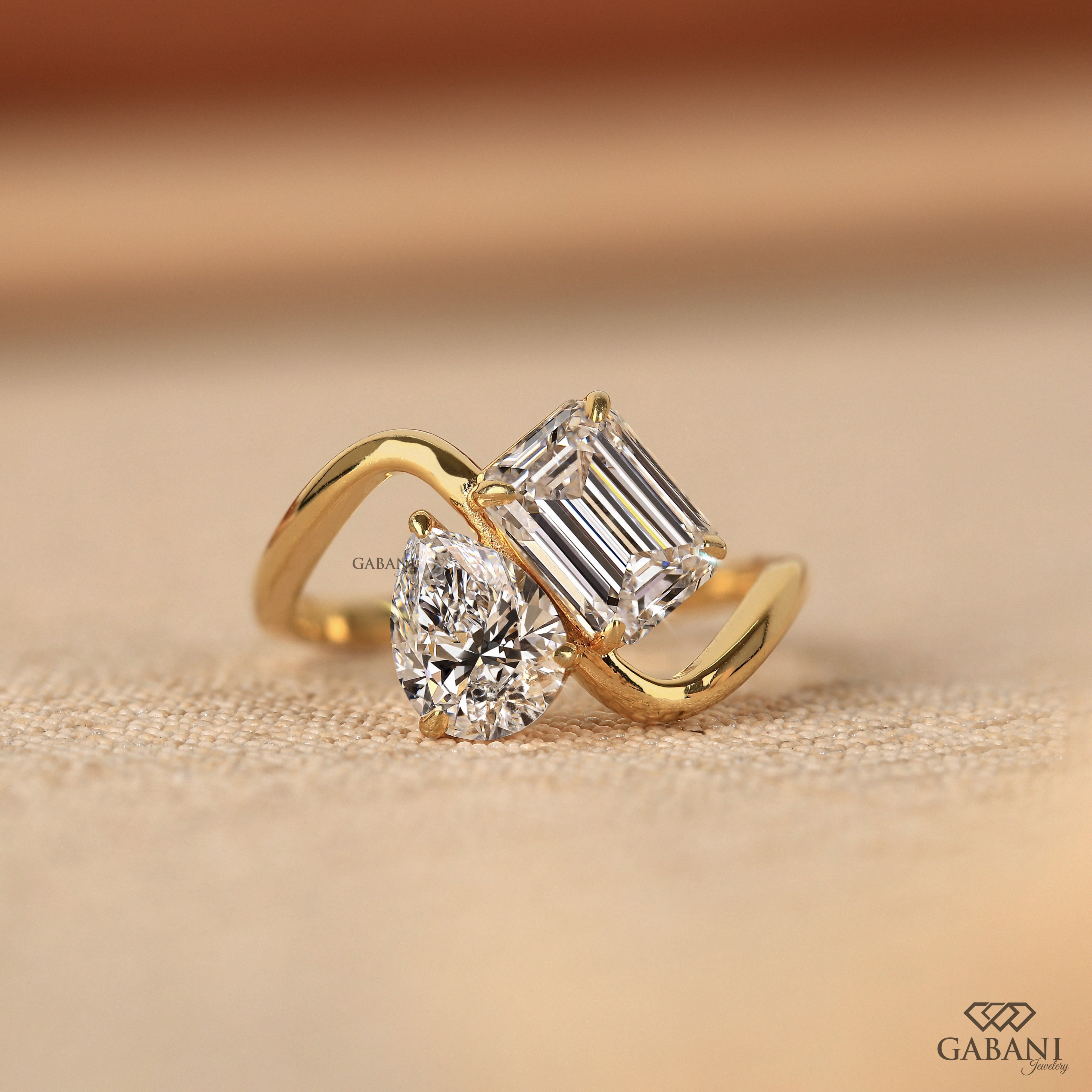 Pear and emerald cut lab grown diamond Toi et Moi ring with a curved yellow gold band, designed for engagement, anniversary, proposal, and statement wear.