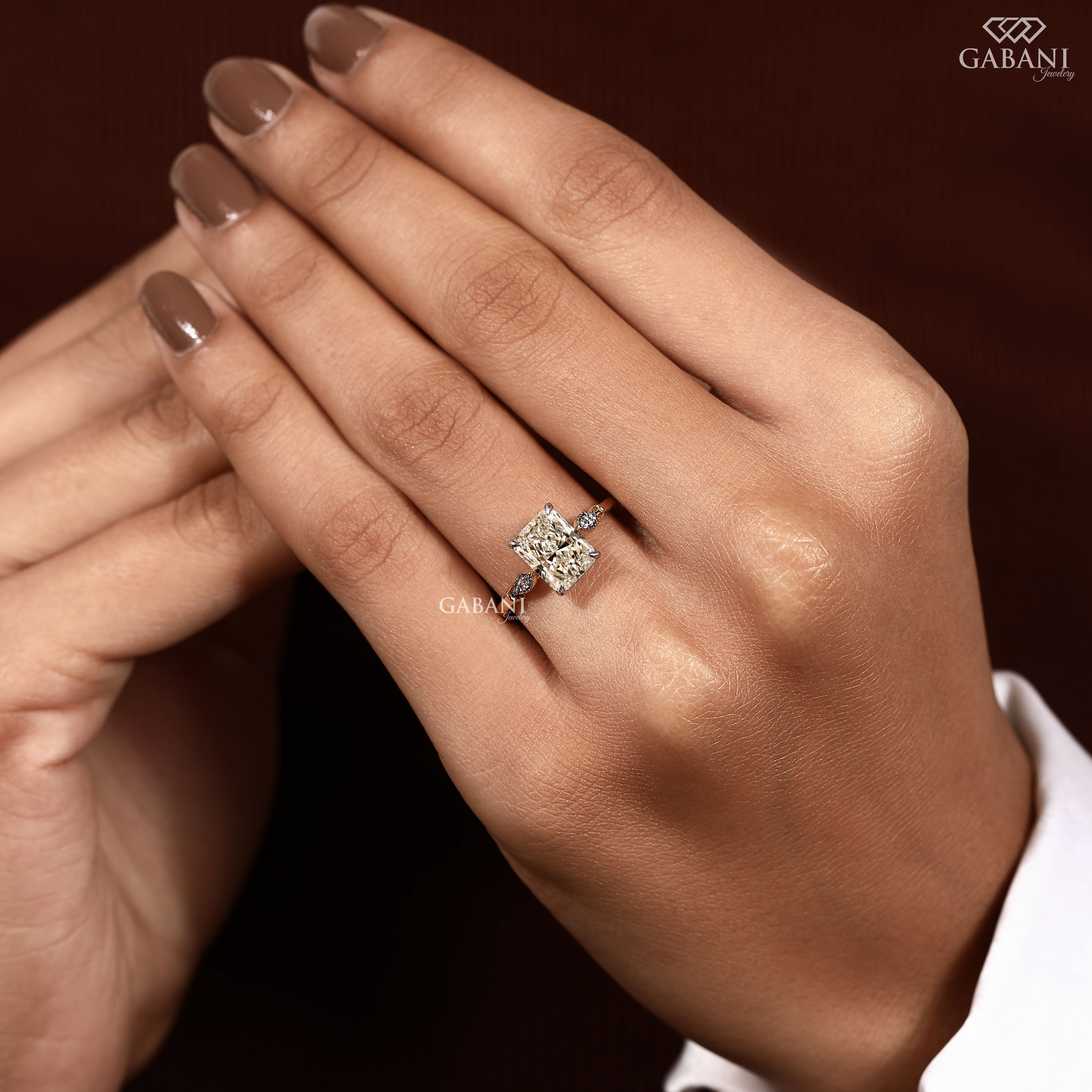 Radiant cut lab grown diamond engagement ring with round side diamond clusters, four prong setting and polished gold band.