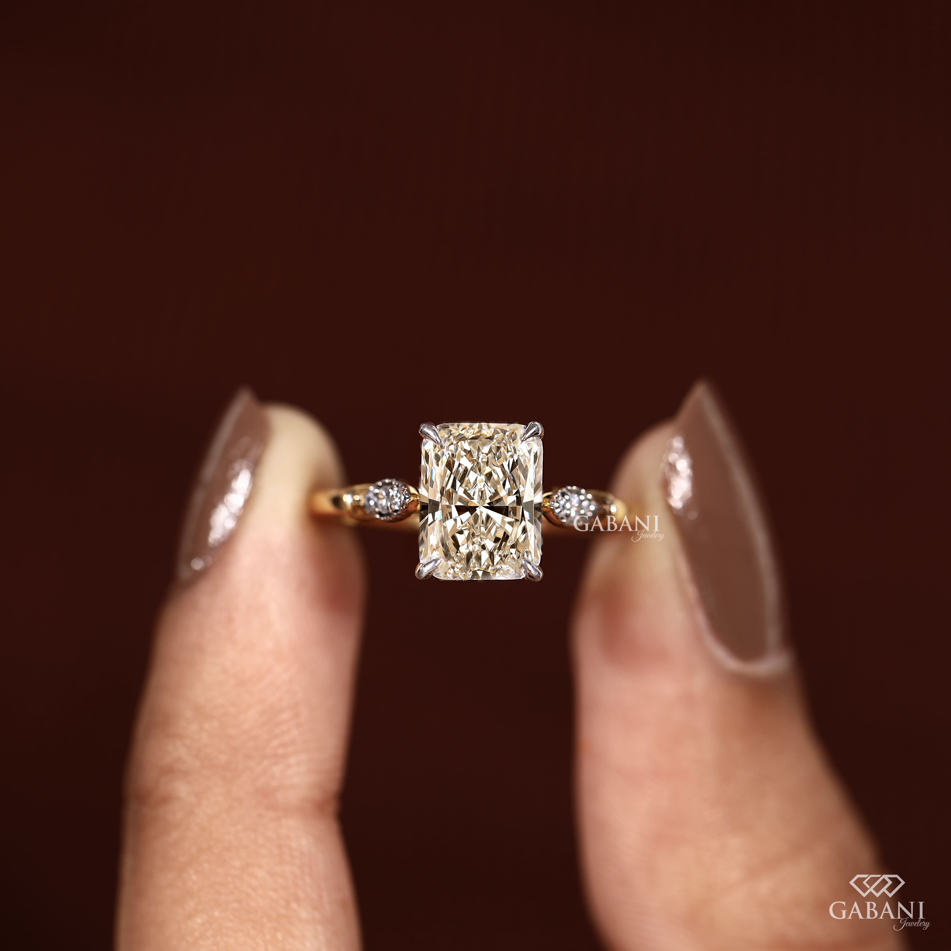 Radiant cut lab grown diamond engagement ring with round side diamond clusters, four prong setting and polished gold band.