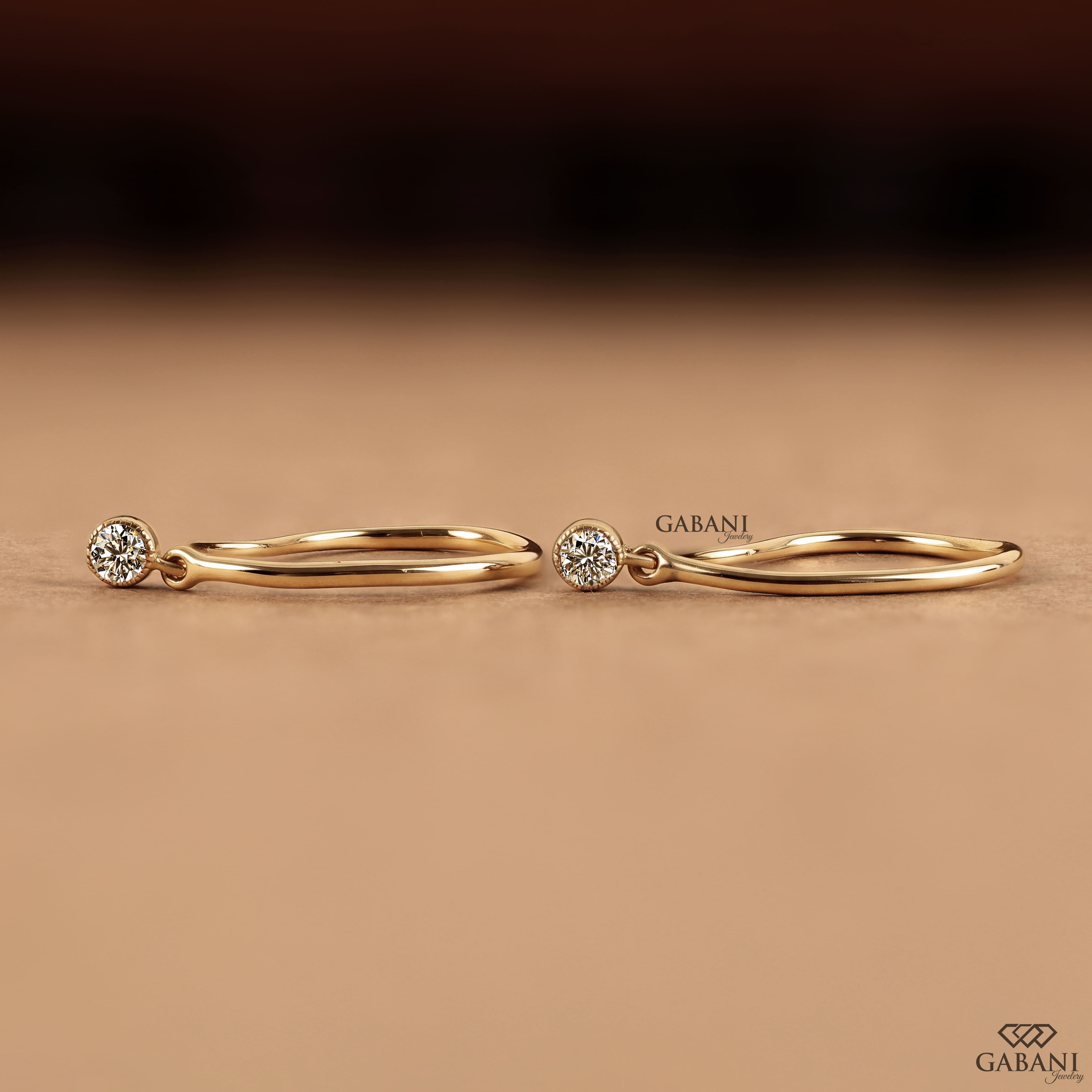 Round cut lab grown diamond hook earrings with 0.10 CTW, bezel set stones and a slim curved gold drop design for everyday wear.