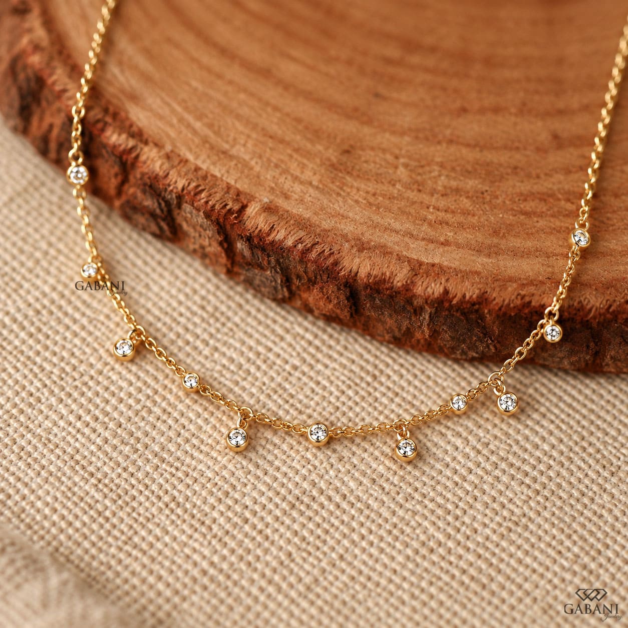 Round cut lab grown diamond station necklace with equal size bezel set diamonds and dangling diamond charms in 18K yellow gold.