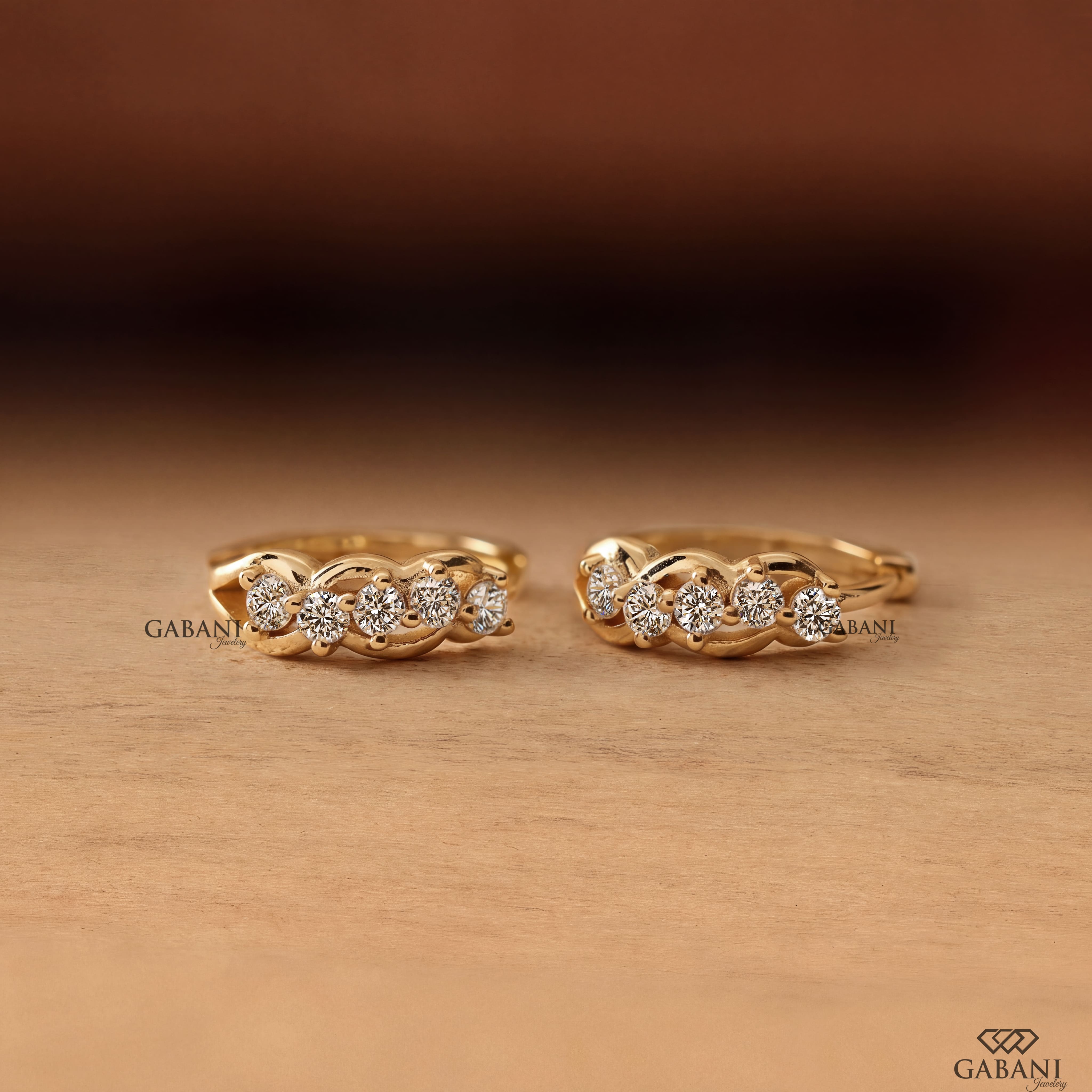 Round diamond infinity huggie hoop earrings in yellow gold with five diamonds and curved gold loop detailing.