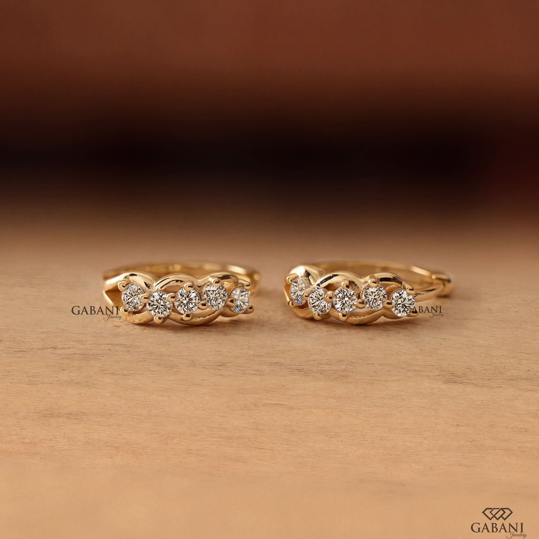 Round diamond infinity huggie hoop earrings in yellow gold with five diamonds and curved gold loop detailing.