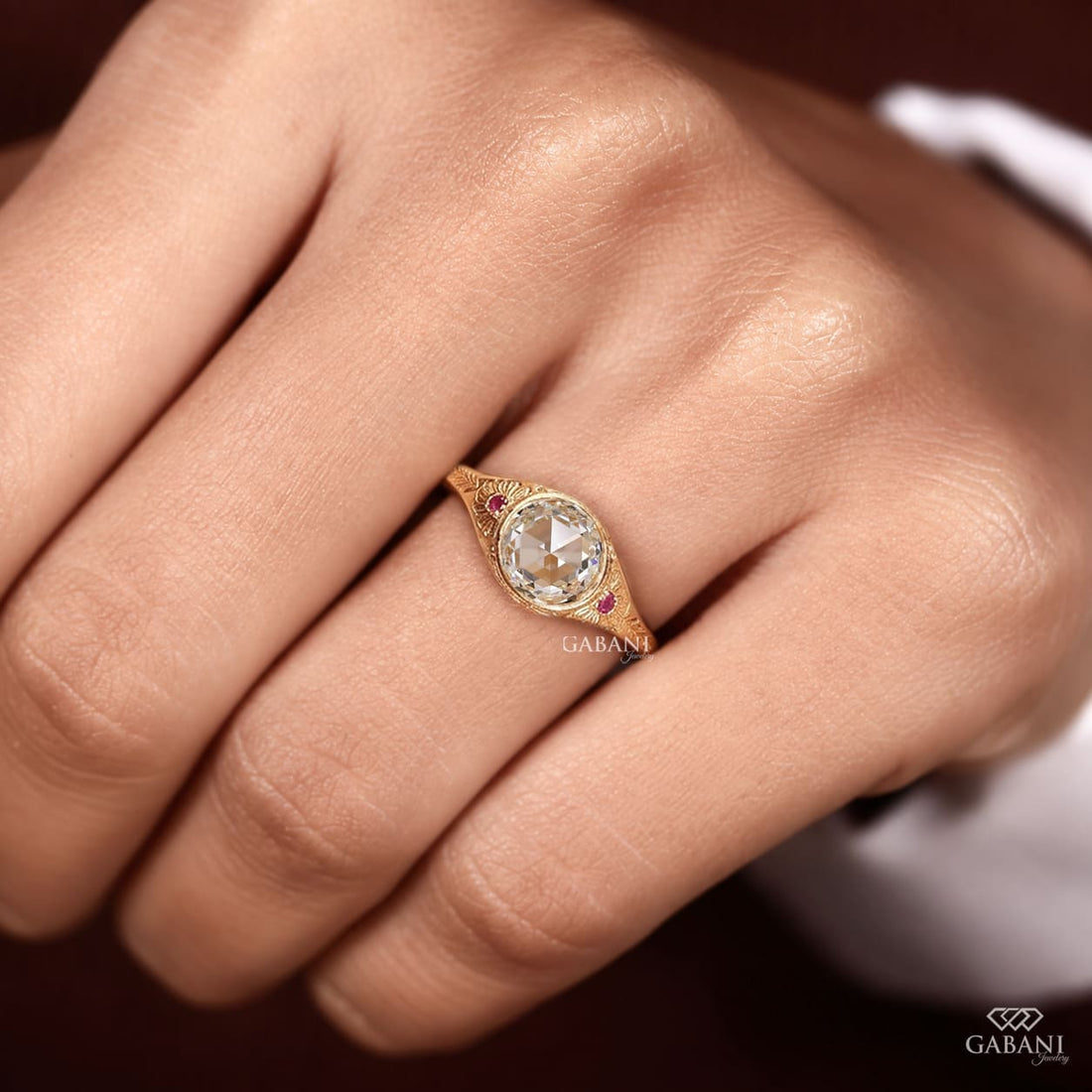 Round rose cut lab grown diamond engagement ring with ruby side accents, floral engraving, and bezel setting in 14K yellow gold.