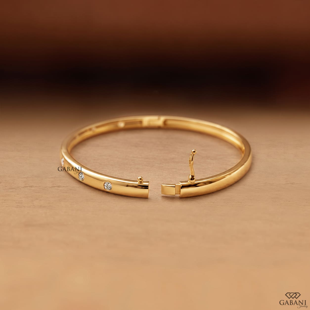 Yellow gold hinged bangle bracelet featuring five round cut diamonds in polished bezel settings along a sleek band.