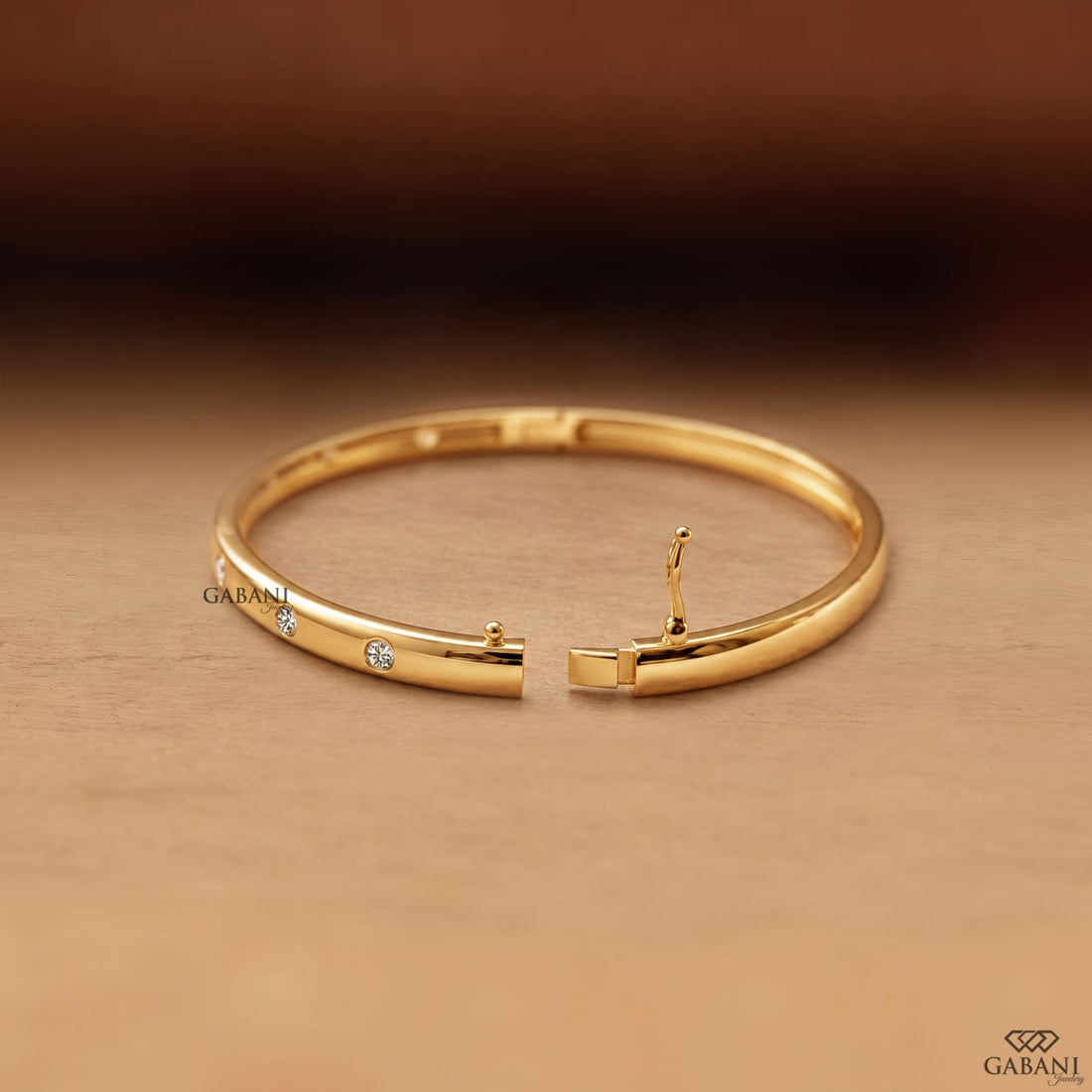 Yellow gold hinged bangle bracelet featuring five round cut diamonds in polished bezel settings along a sleek band.