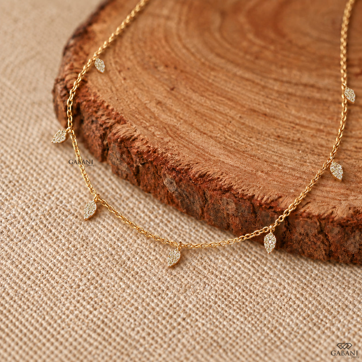 Yellow gold station necklace with multiple dangling pavé diamond leaf charms and a delicate chain, displayed on a wooden surface.