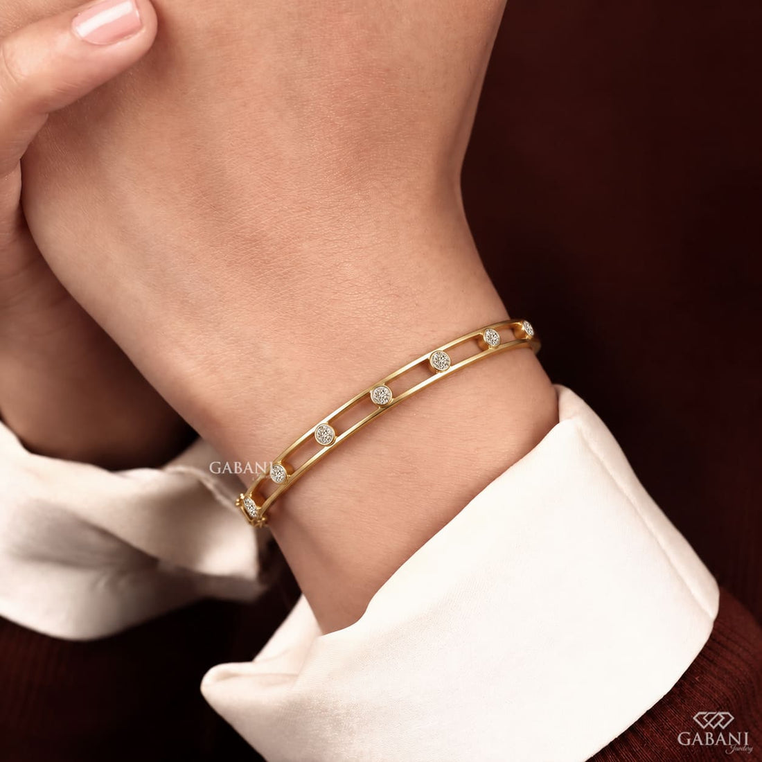 a round lab grown diamond bangle bracelet in yellow gold, featuring evenly spaced bezel set diamonds between two polished gold rails in a modern open-frame design by Gabani Jewelry.