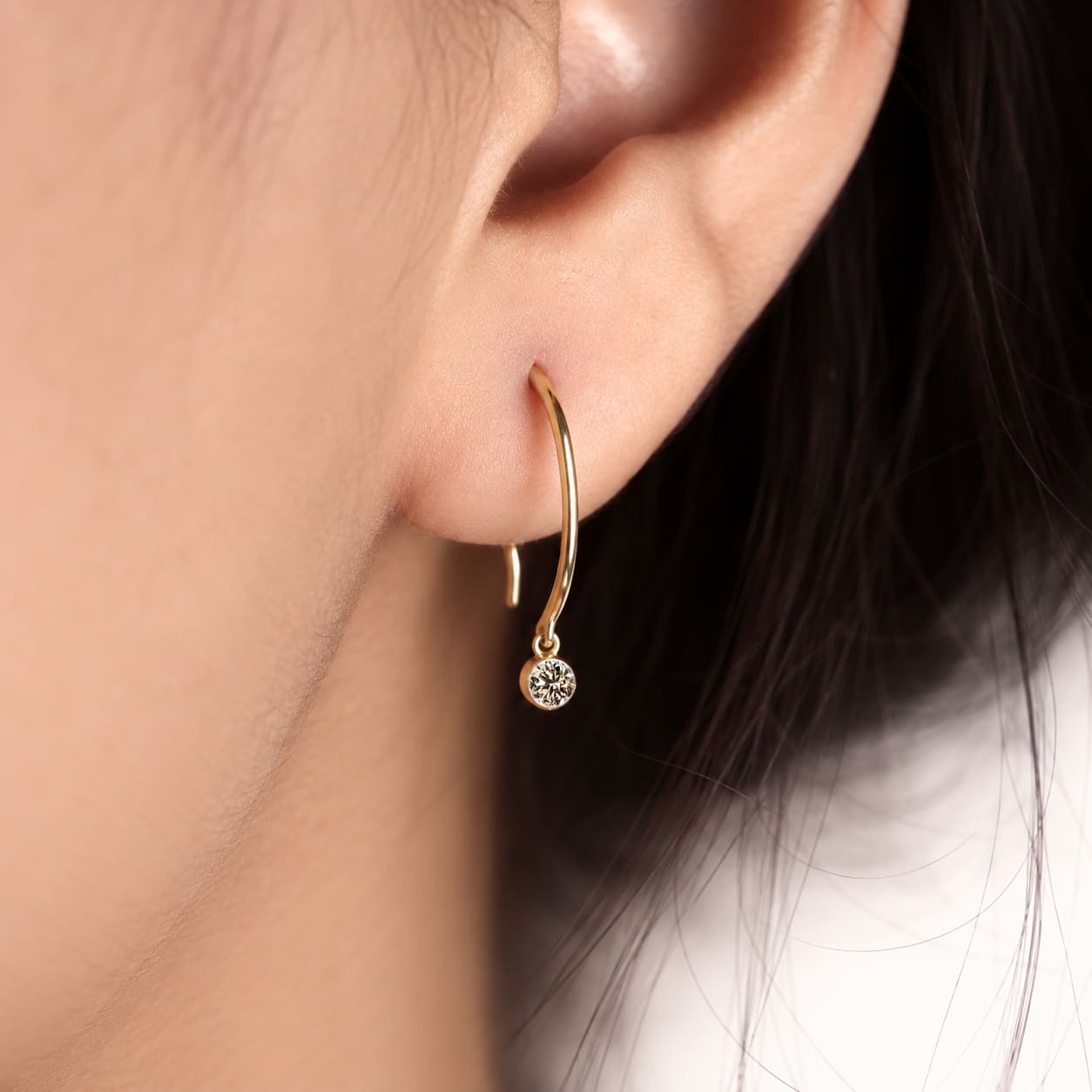 Round cut lab grown diamond hook earrings with 0.10 CTW, bezel set stones and a slim curved gold drop design for everyday wear.