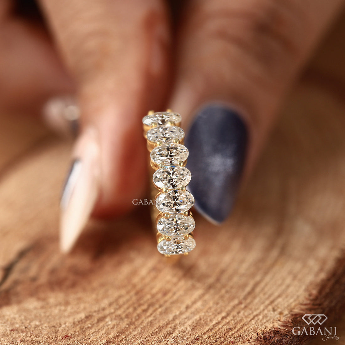 seven oval cut lab grown diamonds arranged in a prong set half eternity wedding band with polished 14K yellow gold.