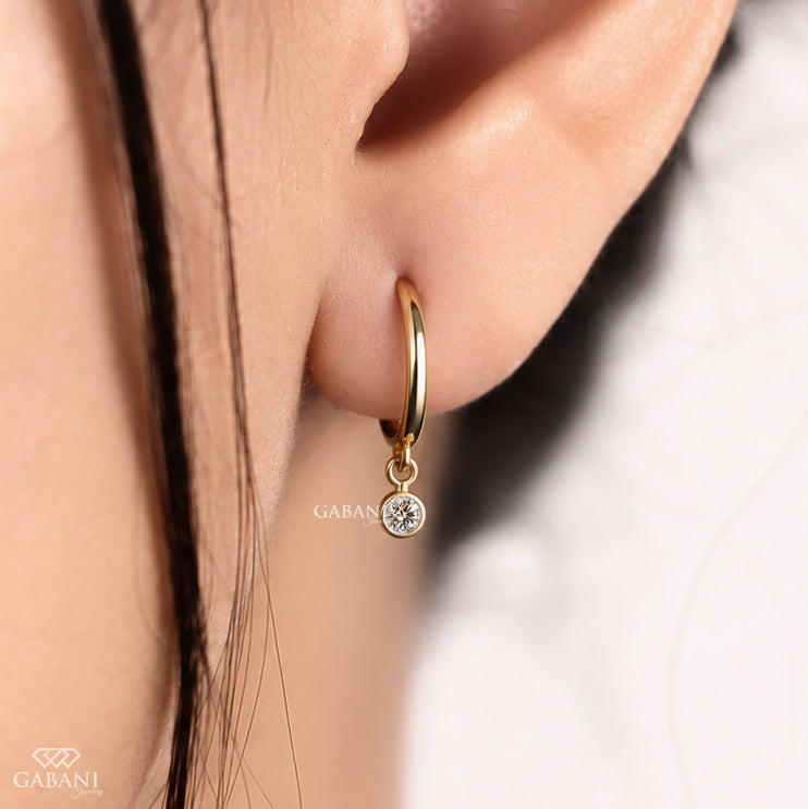 Round lab grown diamond bezel drop huggie earrings in yellow gold with 5 mm diamonds and hinged hoop closure.