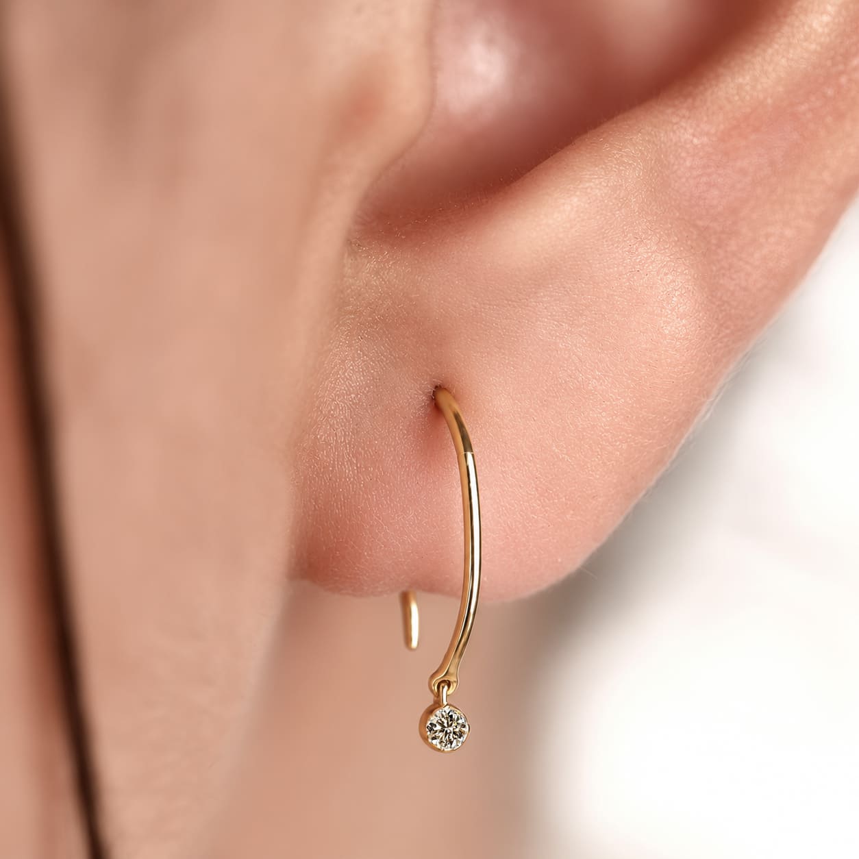 Round cut lab grown diamond hook earrings with 0.10 CTW, bezel set stones and a slim curved gold drop design for everyday wear.