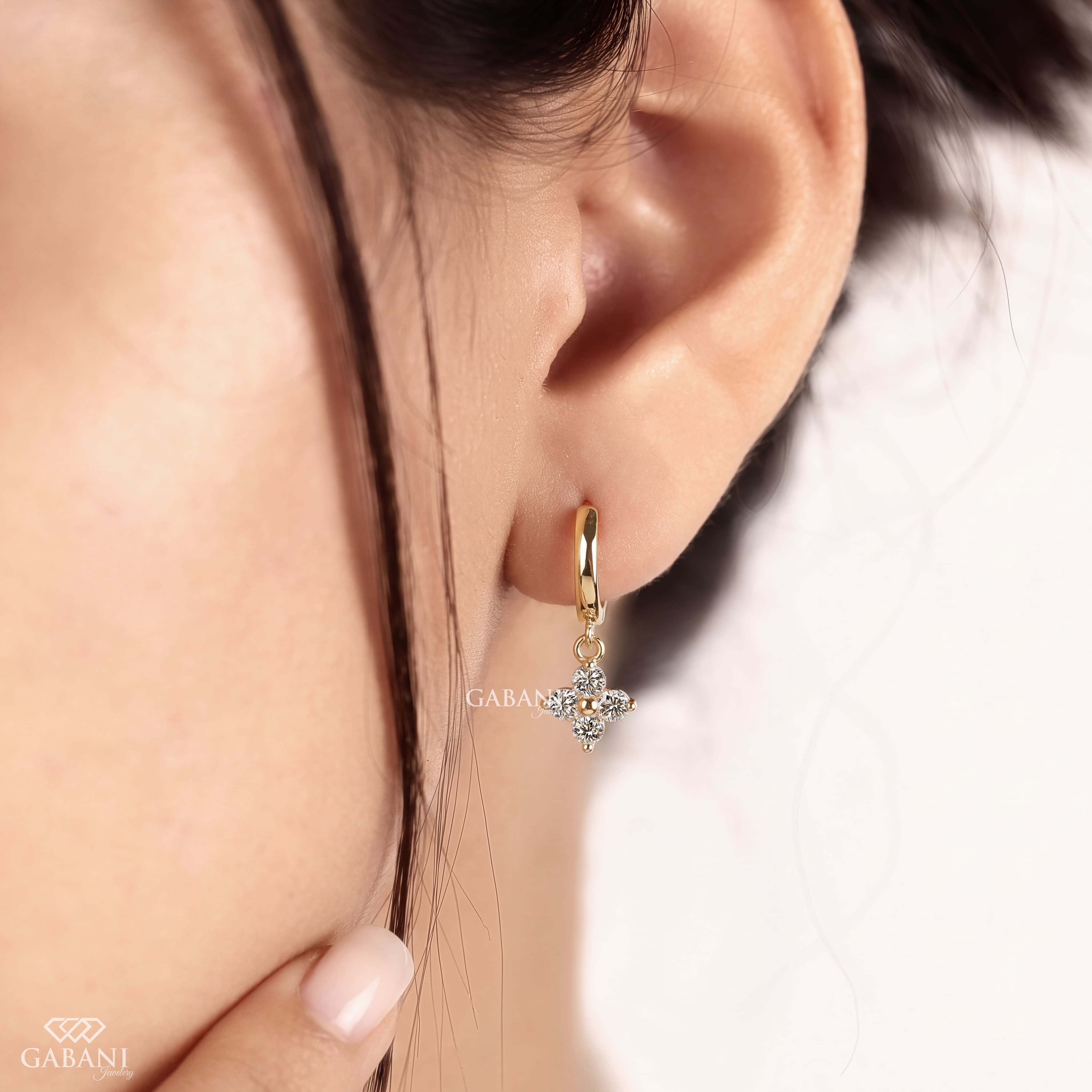 Close-up of round cut lab grown diamond flower charm huggie hoop earrings with four stone floral clusters in polished 18K yellow gold.