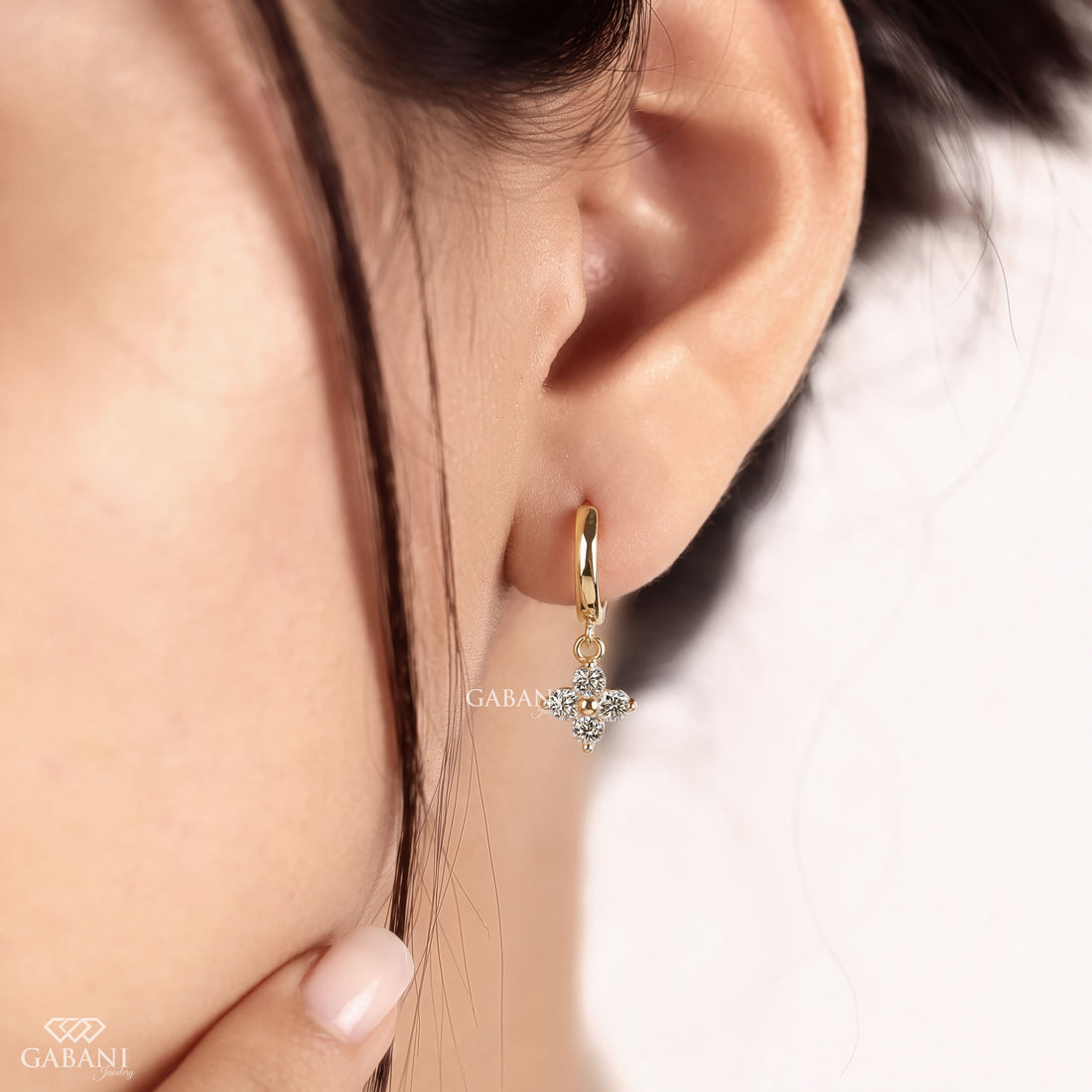 Close-up of round cut lab grown diamond flower charm huggie hoop earrings with four stone floral clusters in polished 18K yellow gold.