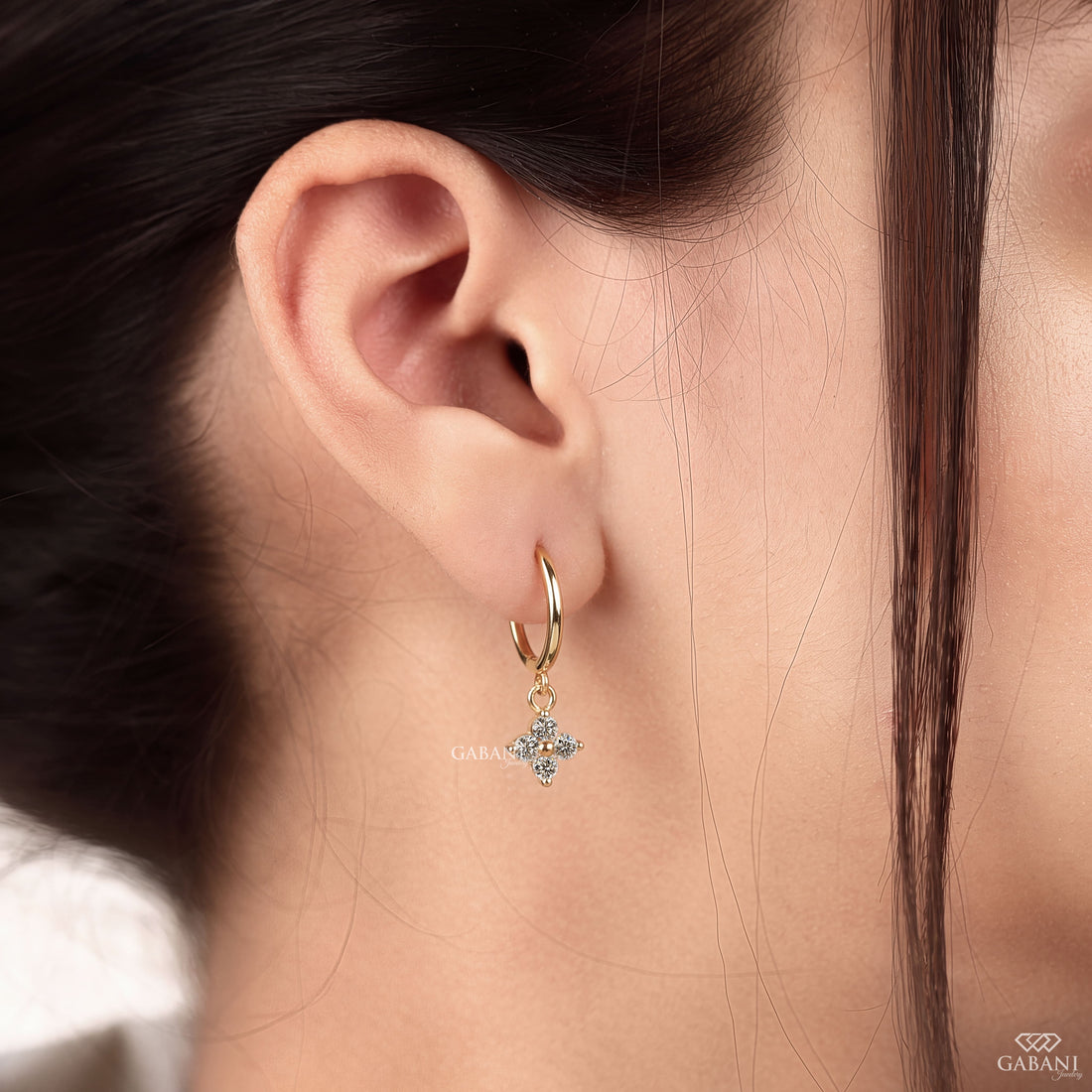 Close-up of round cut lab grown diamond flower charm huggie hoop earrings with four stone floral clusters in polished 18K yellow gold.
