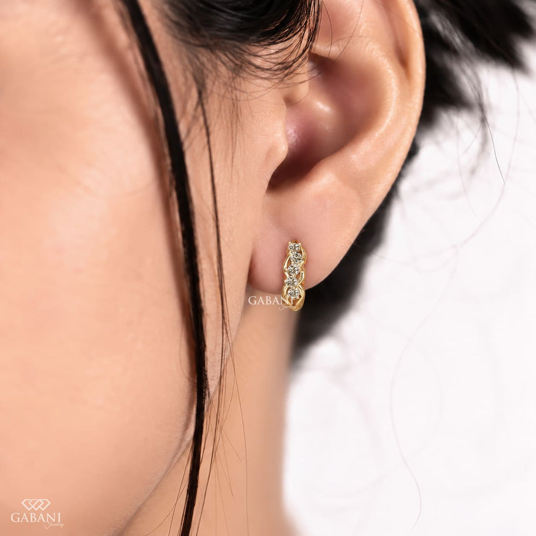 Round diamond infinity huggie hoop earrings in yellow gold with five diamonds and curved gold loop detailing.