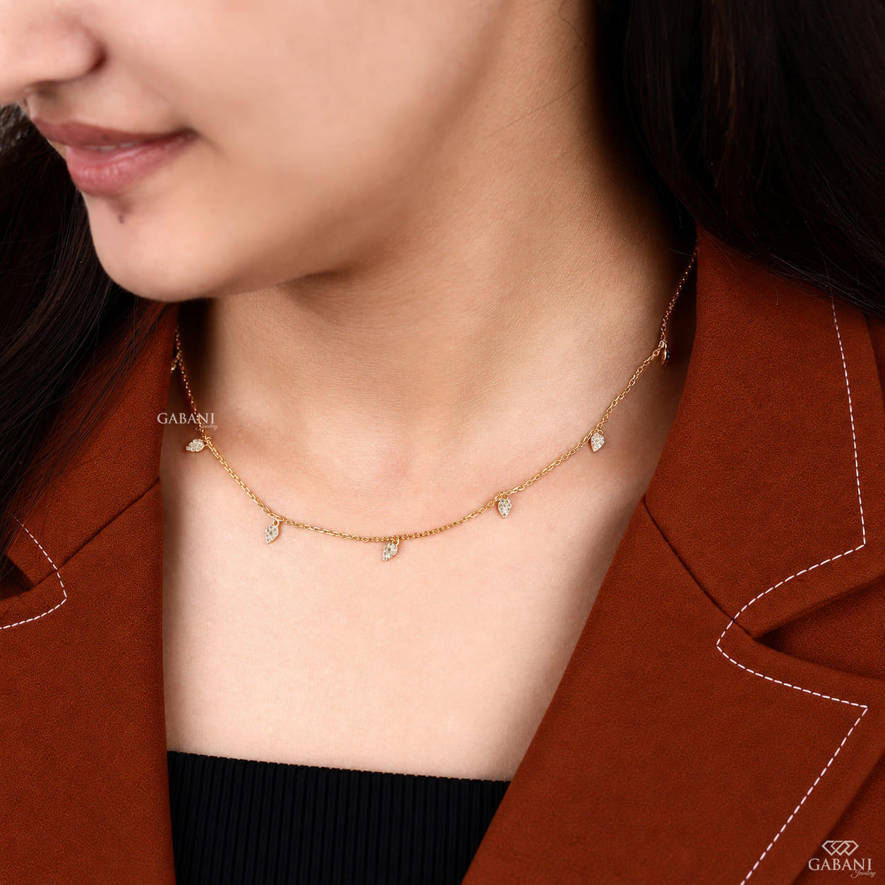 Yellow gold station necklace with multiple dangling pavé diamond leaf charms and a delicate chain, displayed on a wooden surface.