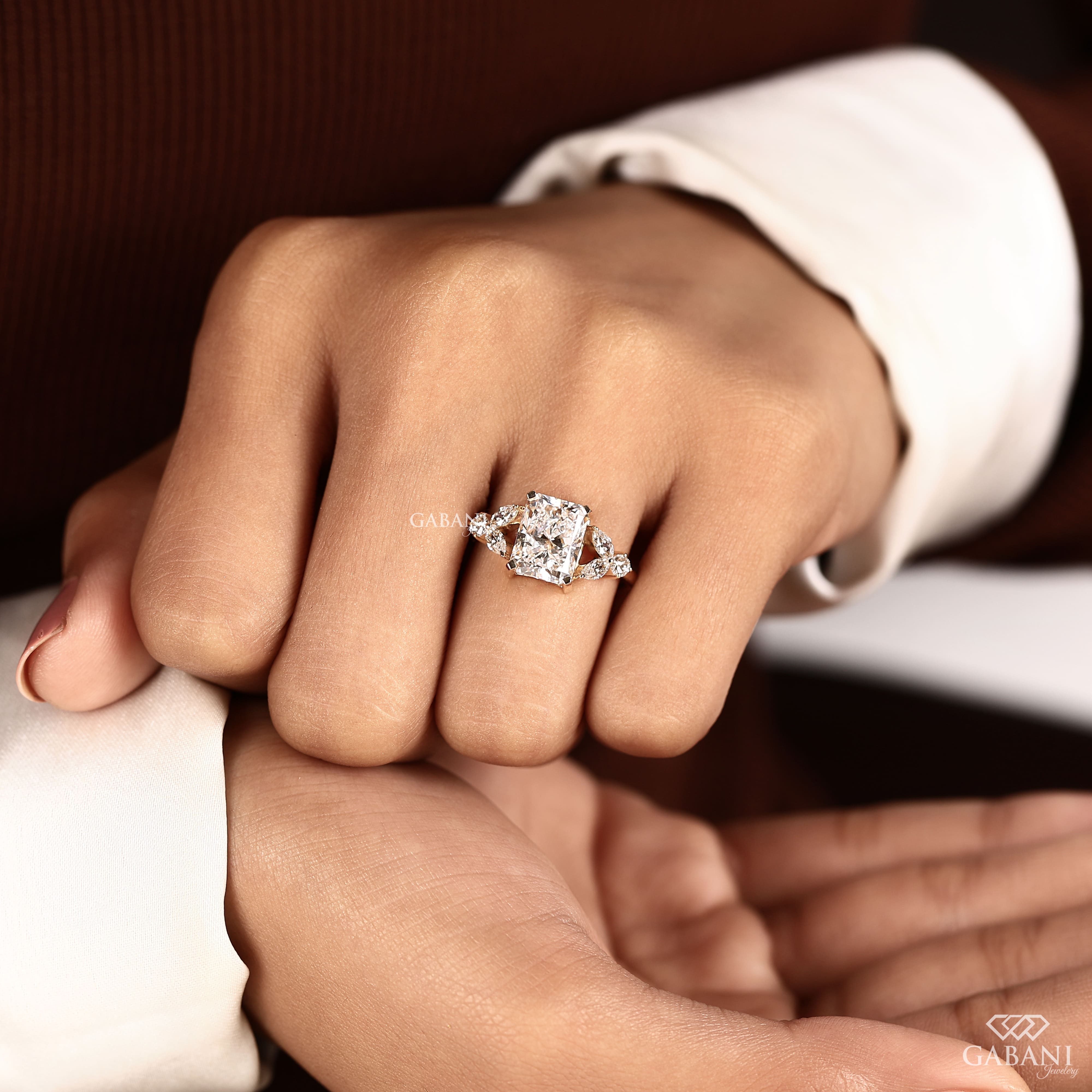 Radiant cut lab grown diamond engagement ring with marquise and round side diamond accents in a nature inspired gold setting.