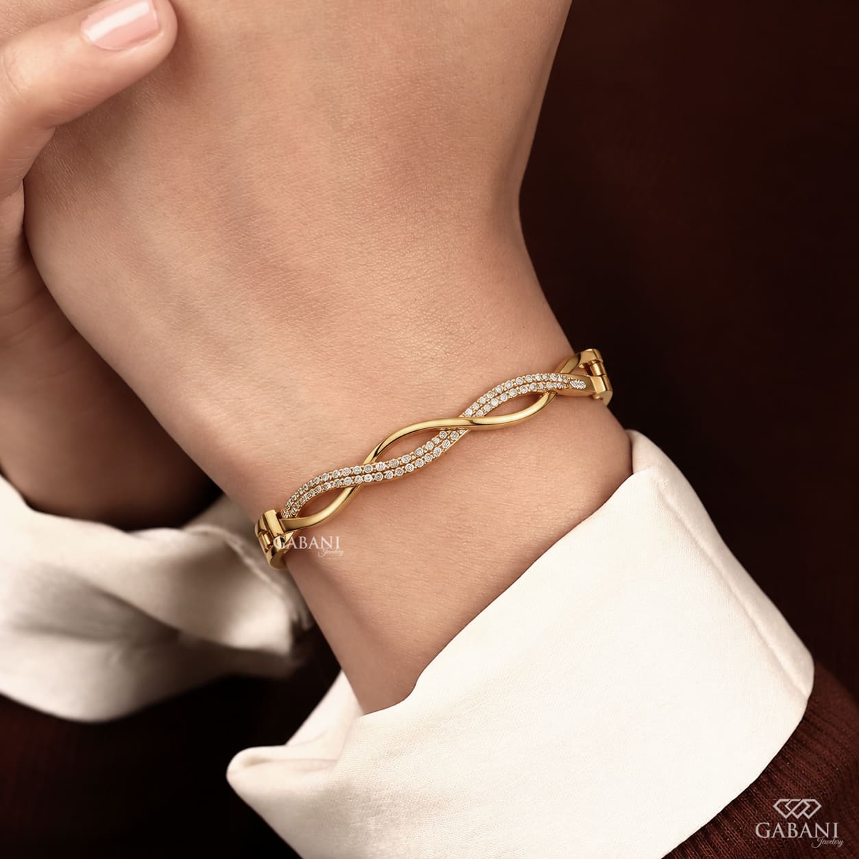 Yellow gold infinity twist bangle bracelet with intertwined polished bands and double rows of round pavé set diamonds.