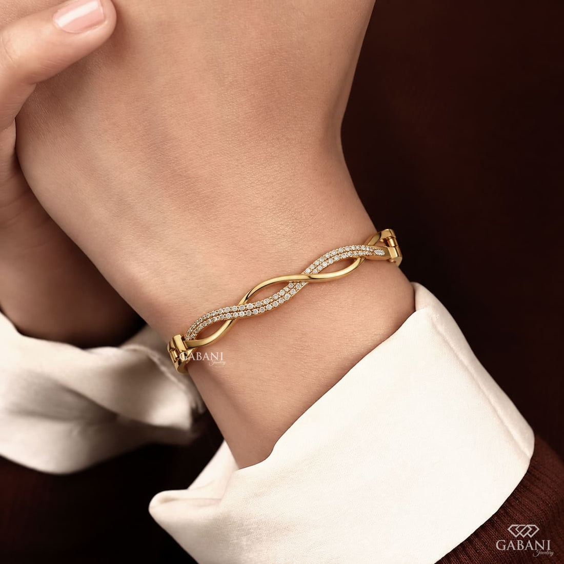 Yellow gold infinity twist bangle bracelet with intertwined polished bands and double rows of round pavé set diamonds.
