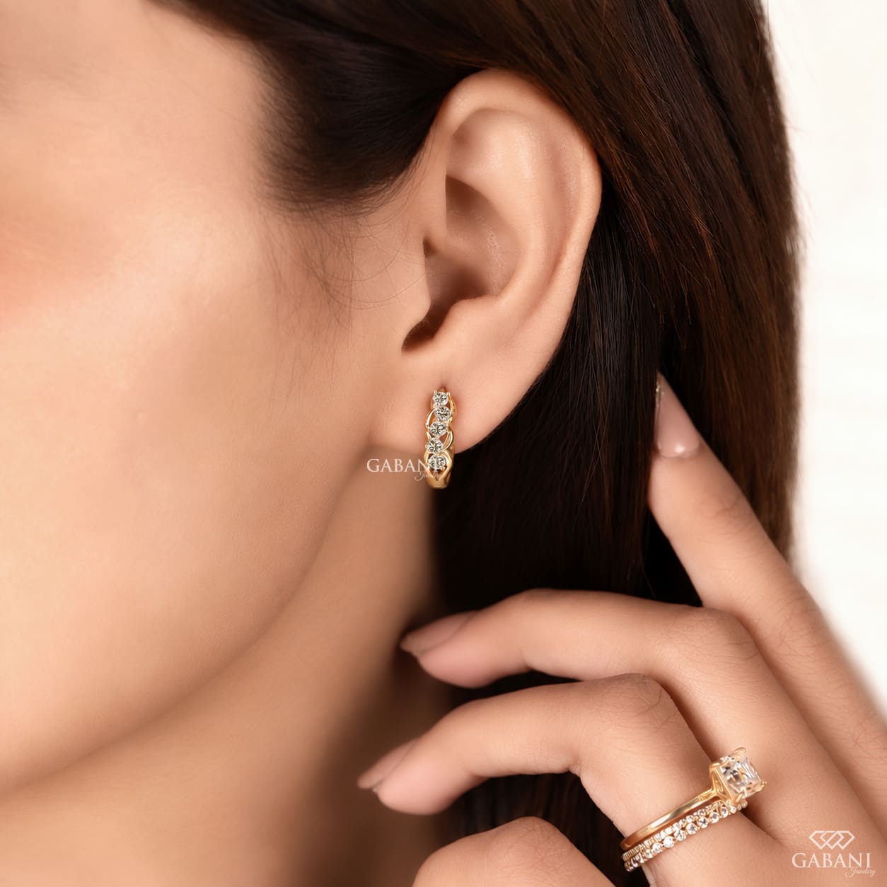 Round diamond infinity huggie hoop earrings in yellow gold with five diamonds and curved gold loop detailing.