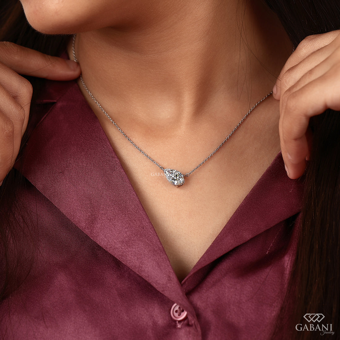 Necklace with a diamond pendant worn by a person in a burgundy shirt, with 'GABANI' branding.