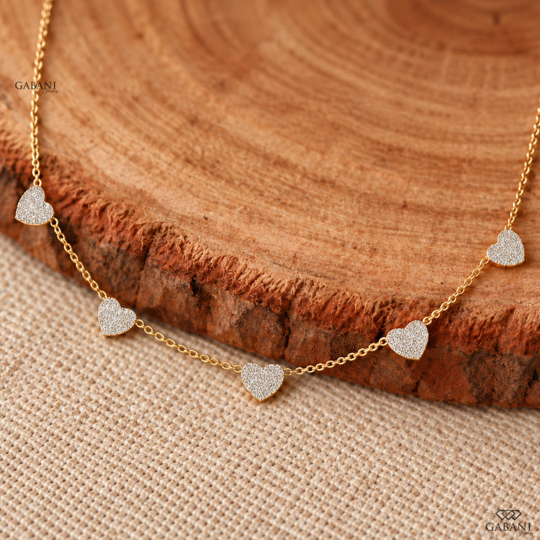 Dainty gold necklace with five sparkling heart charms covered in small round pavé set diamonds on a fine chain.
