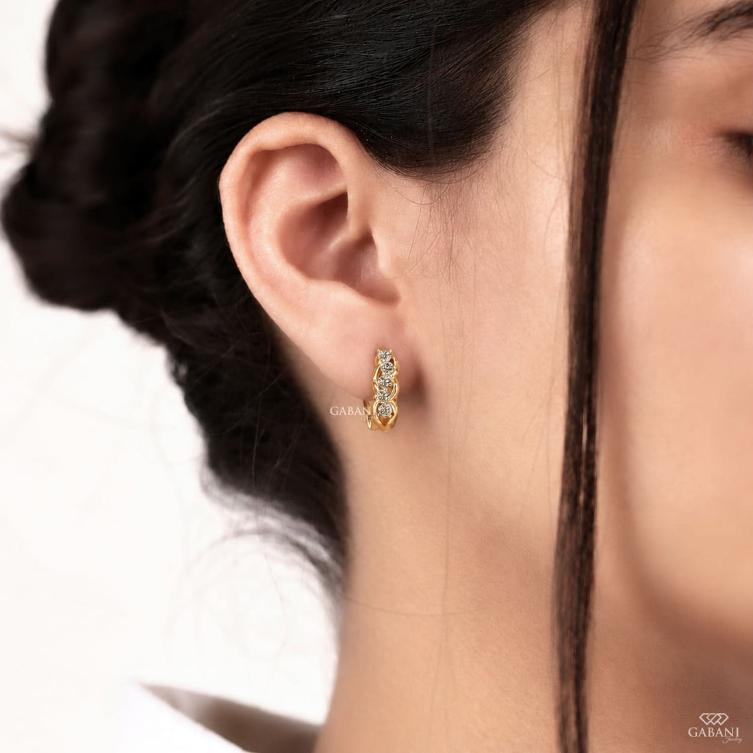 Round diamond infinity huggie hoop earrings in yellow gold with five diamonds and curved gold loop detailing.