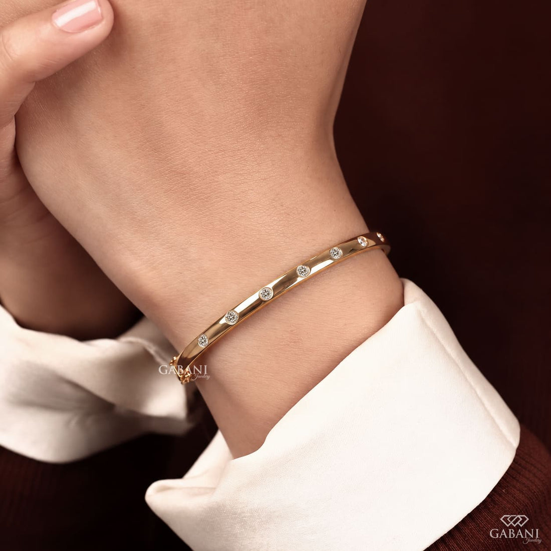 Yellow gold hinged bangle bracelet featuring five round cut diamonds in polished bezel settings along a sleek band.