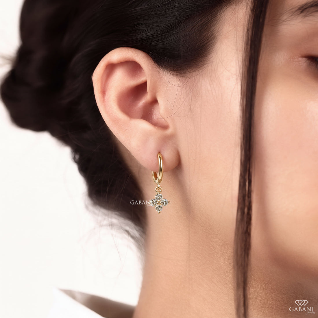 Close-up of round cut lab grown diamond flower charm huggie hoop earrings with four stone floral clusters in polished 18K yellow gold.