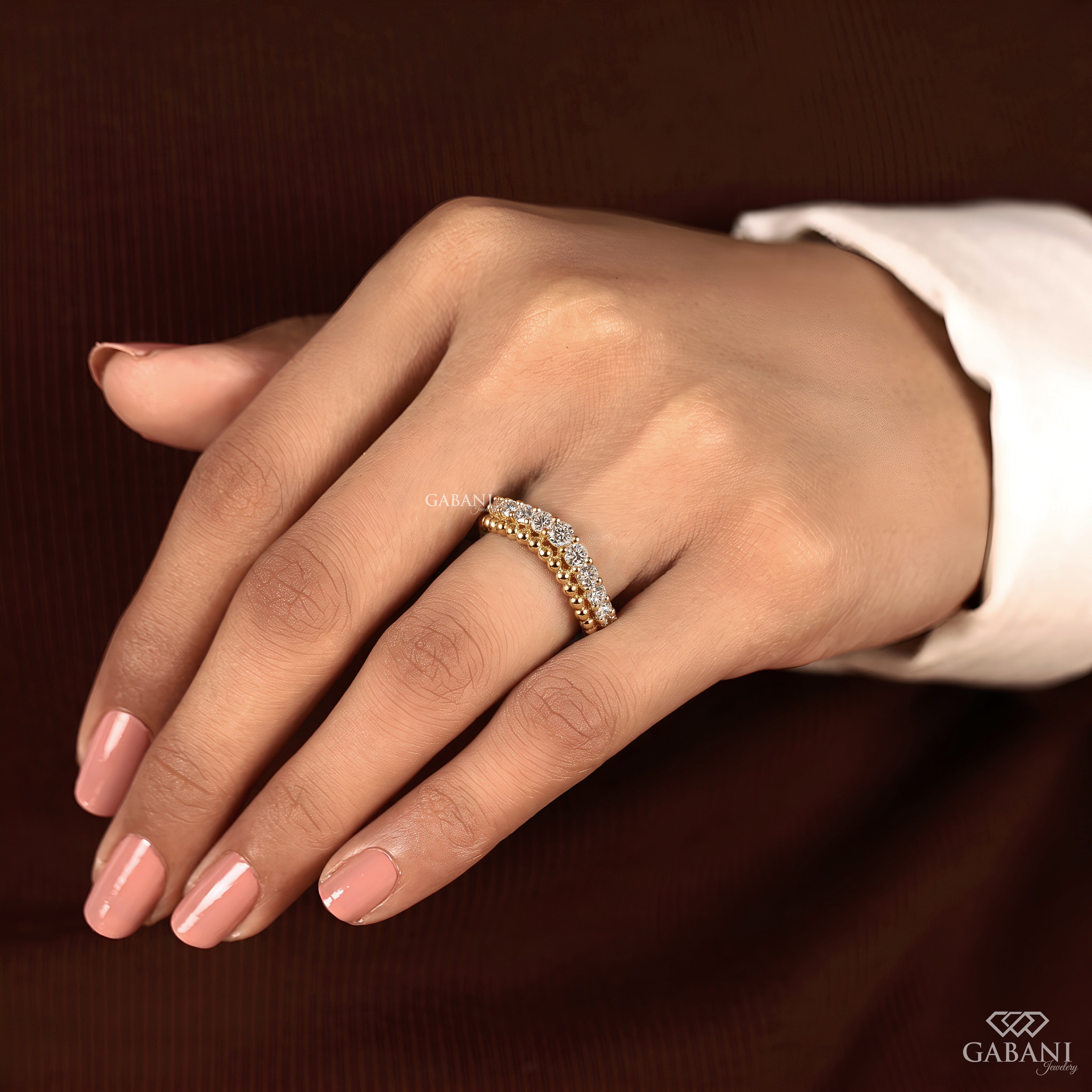 A close-up of a hand wearing a delicate triple-row diamond ring with alternating yellow gold and white diamonds, set against a dark brown background.