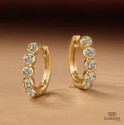 Graduated round diamond bezel huggie earrings in yellow gold with five round diamonds and a hinged hoop closure.
