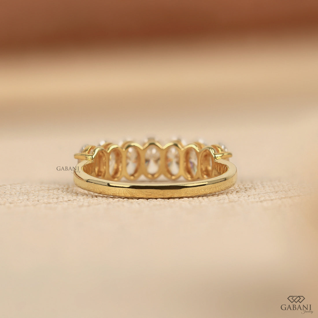 seven oval cut lab grown diamonds arranged in a prong set half eternity wedding band with polished 14K yellow gold.