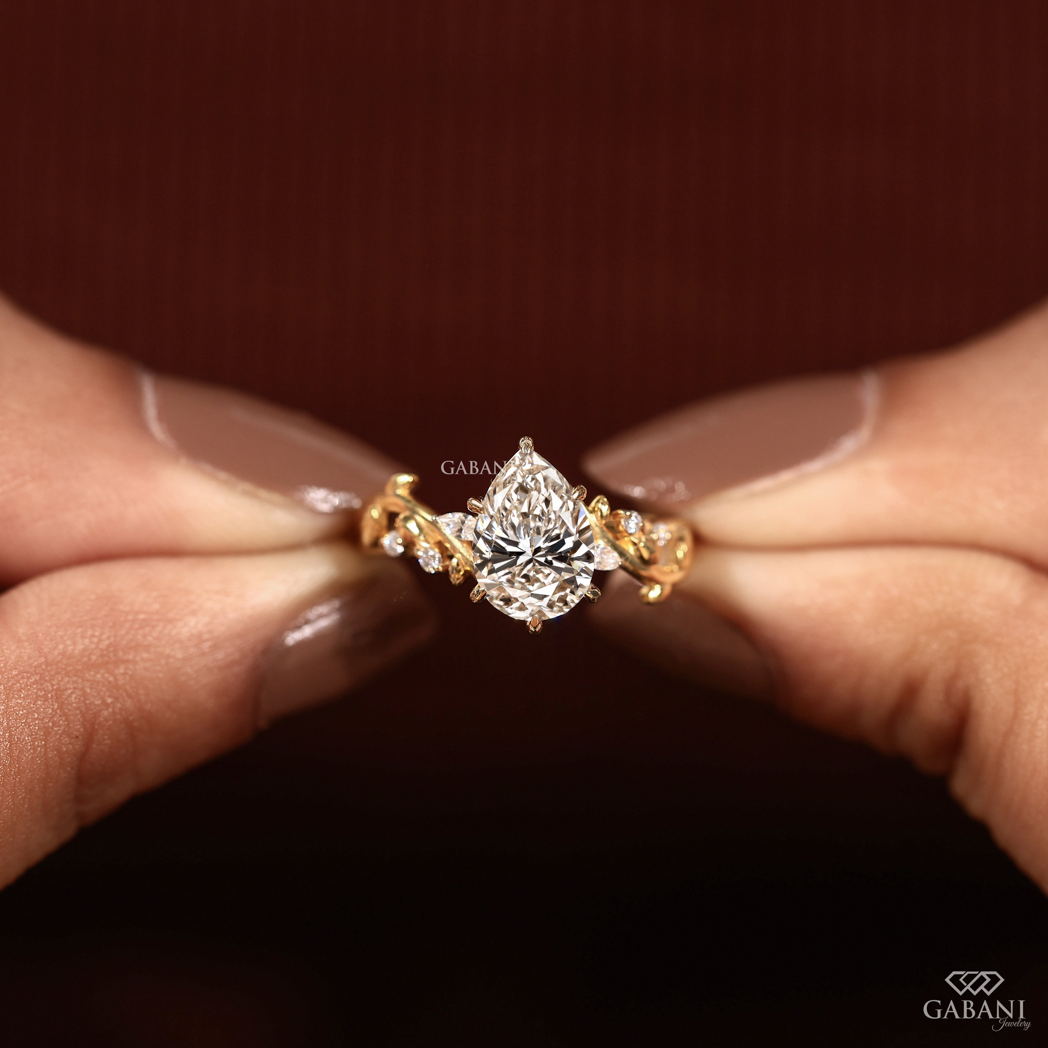 Holding pear cut lab grown diamond leaf style engagement ring in fingers