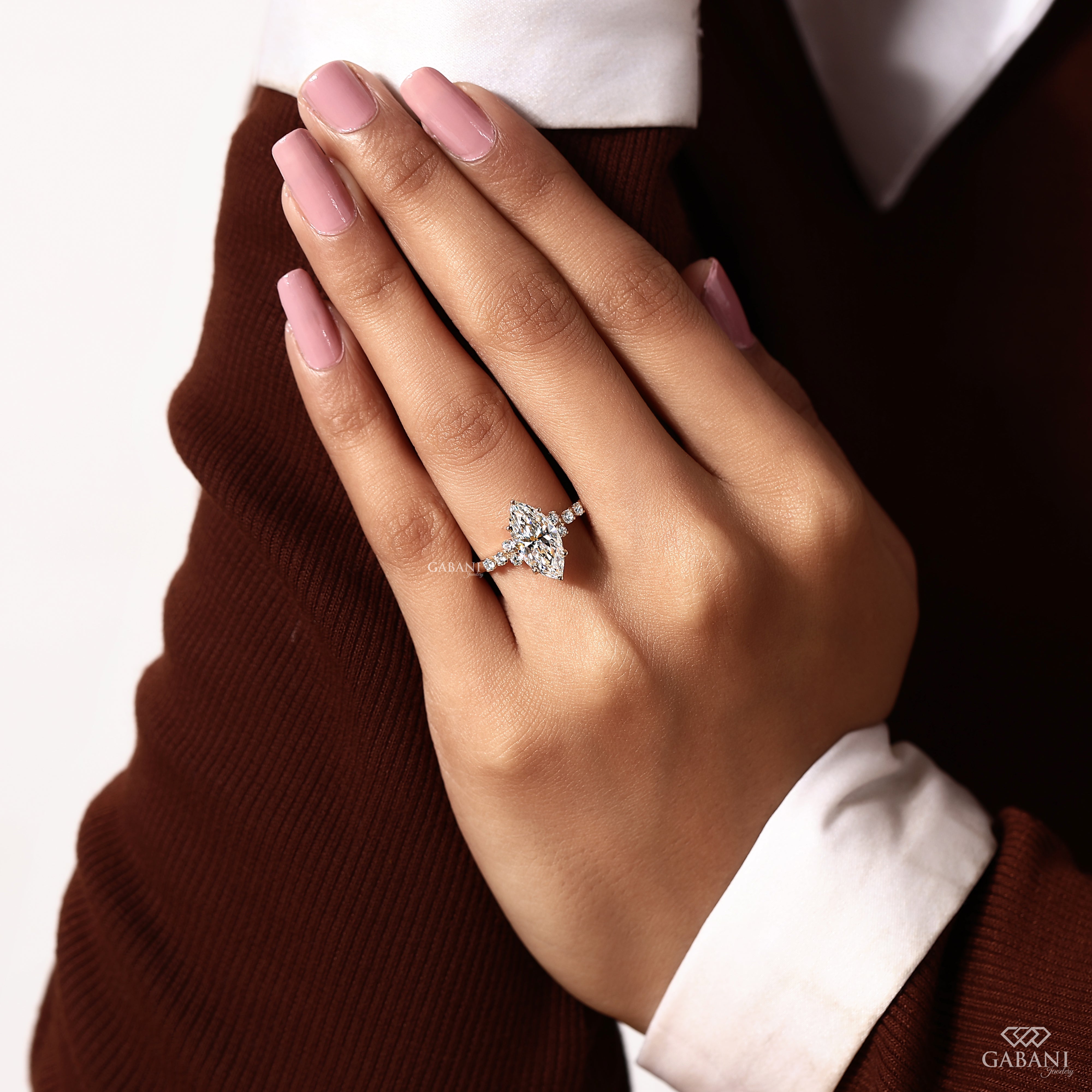 A close-up of a hand wearing a sparkling four-leaf clover ring with a pavé band, styled with a brown sweater and white shirt cuff.