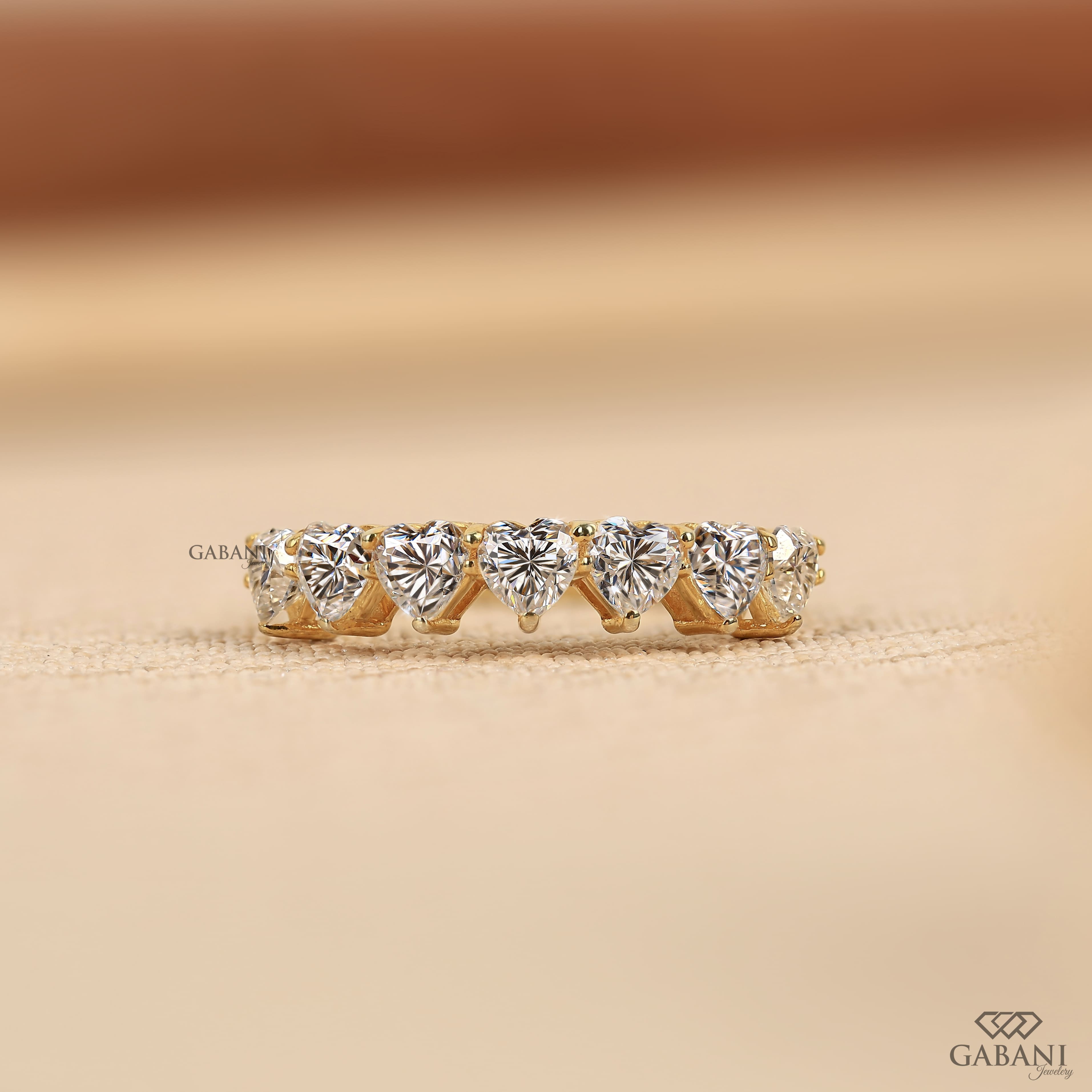 seven heart cut lab grown diamonds in a yellow gold half eternity wedding band with delicate prong settings.
