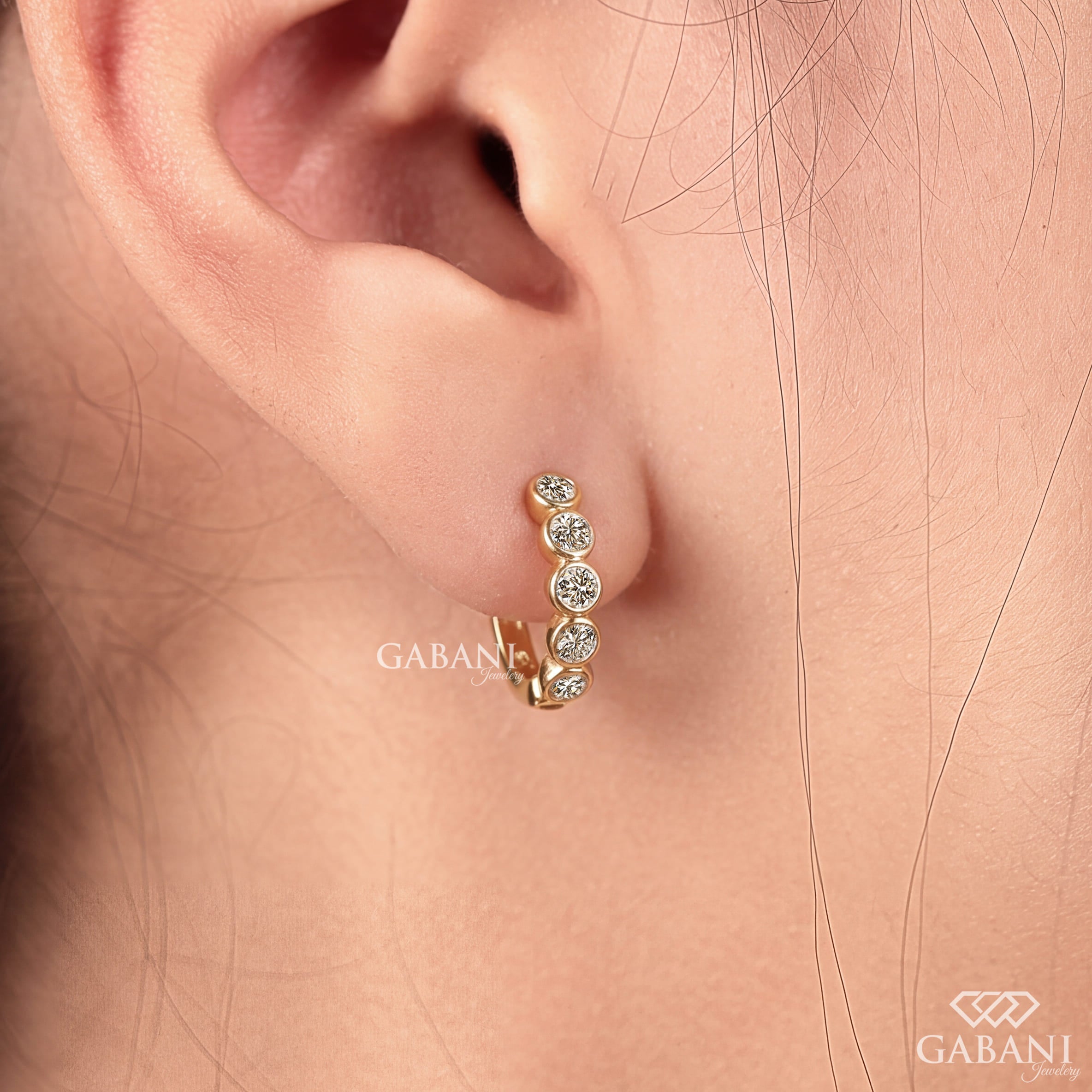 Graduated round diamond bezel huggie earrings in yellow gold with five round diamonds and a hinged hoop closure.